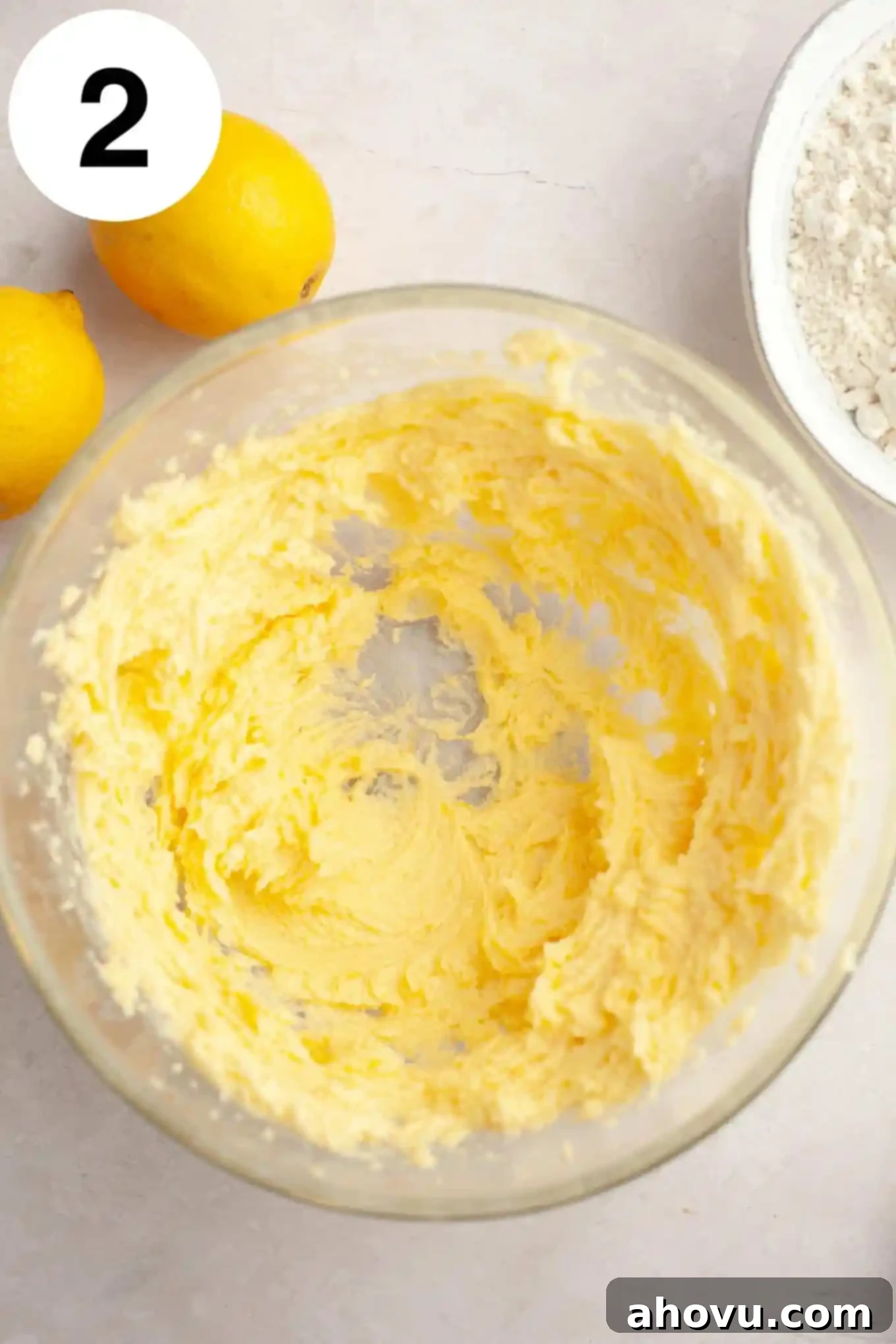 An overhead view of a perfectly creamed mixture of butter, granulated sugar, and lemon zest in a glass mixing bowl, light and fluffy.