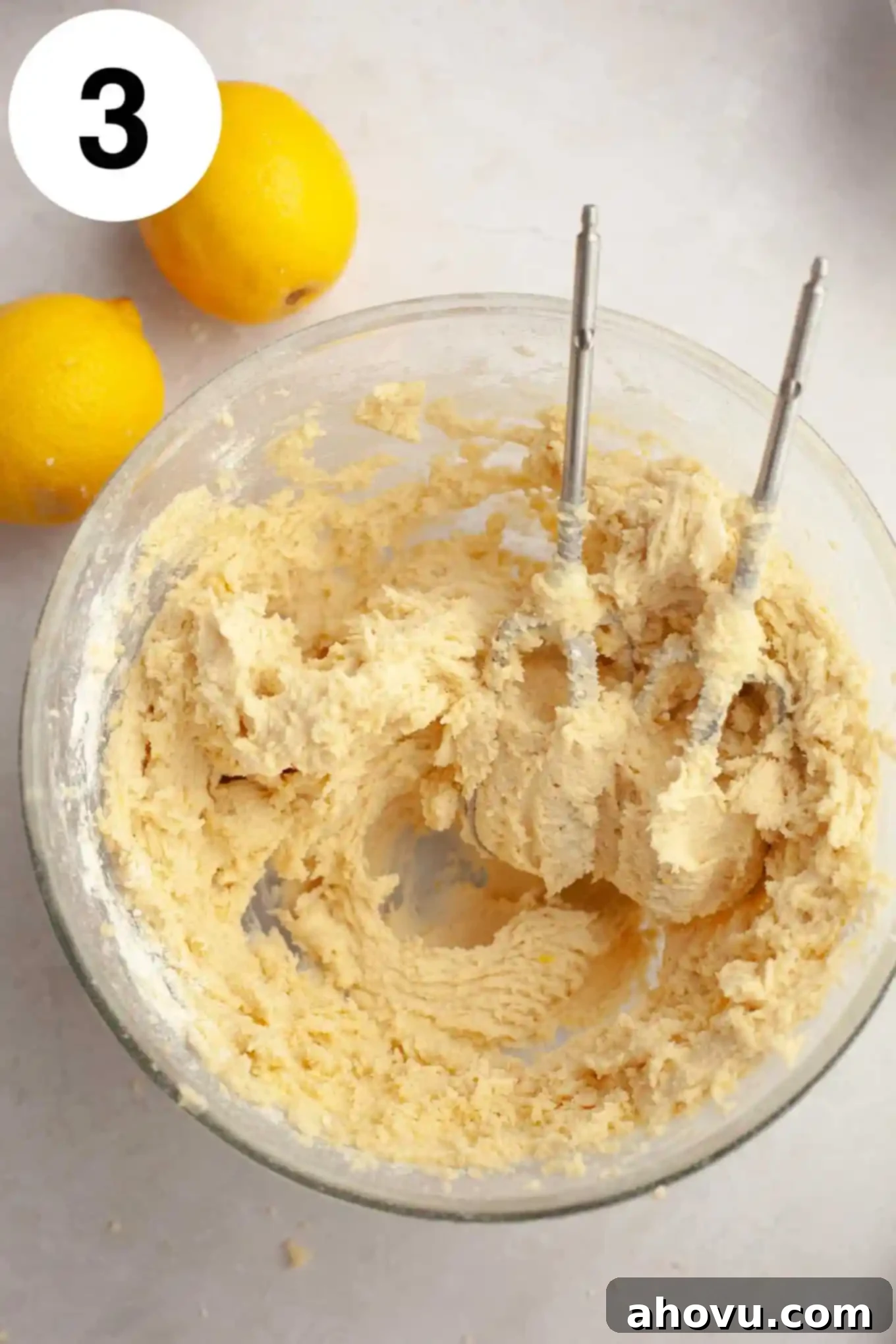 An overhead view of freshly prepared lemon cookie dough, with small specks of lemon zest visible, resting in a glass mixing bowl.
