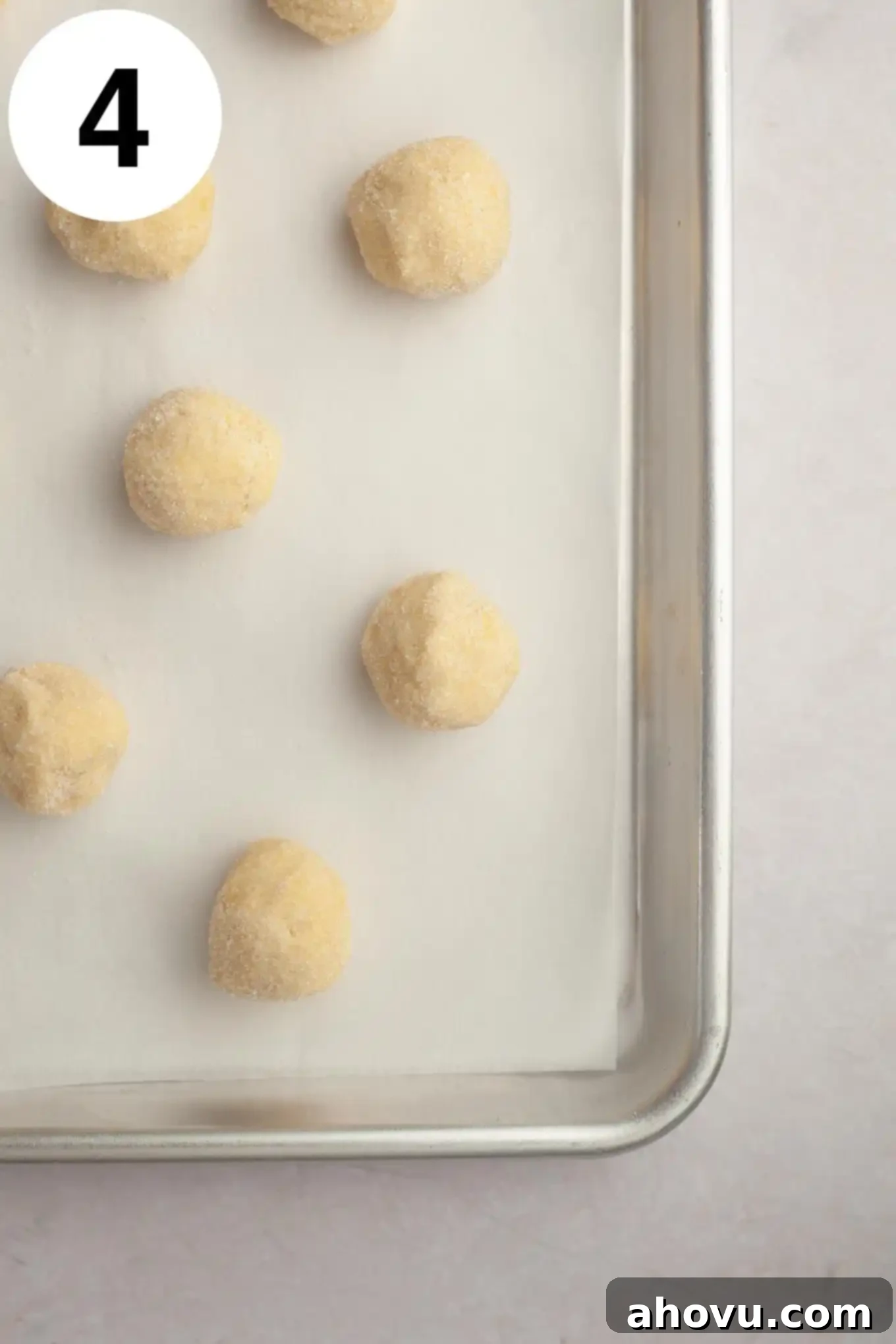An overhead view of perfectly rolled lemon cookie dough balls, lightly coated in granulated sugar, arranged neatly on a parchment-lined baking sheet before baking.