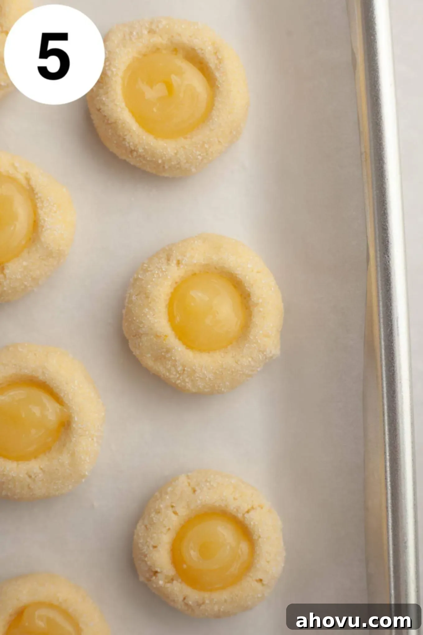 An overhead view of unbaked lemon cookie dough balls with perfect indentations, each precisely filled with vibrant lemon curd, awaiting baking.