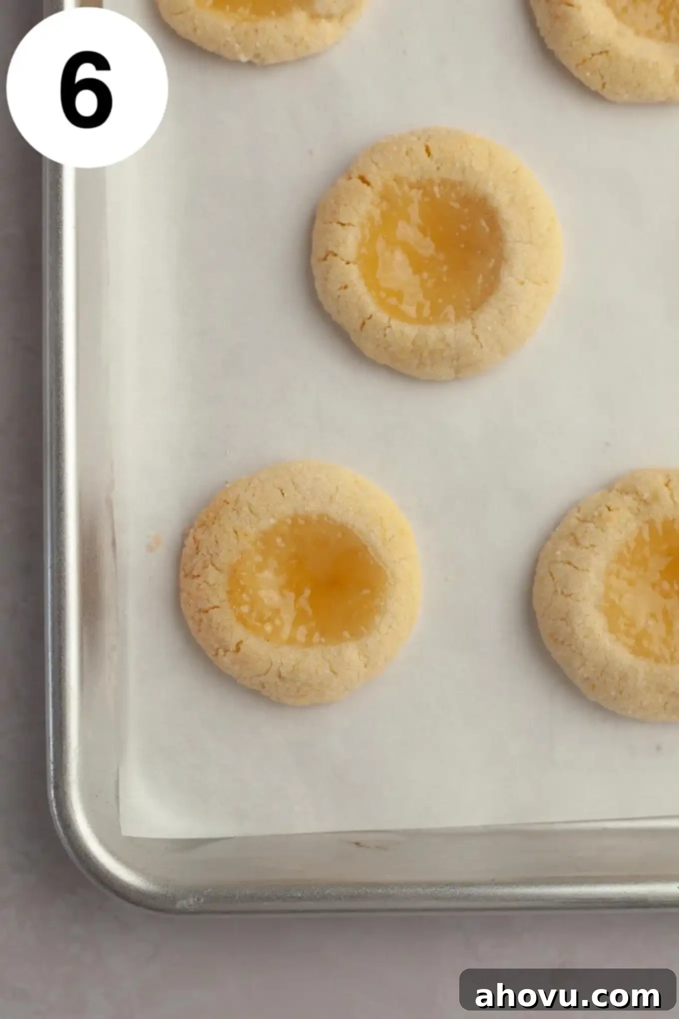 An overhead view of freshly baked lemon curd cookies, golden brown around the edges with set lemon curd, cooling on a parchment-lined baking sheet.