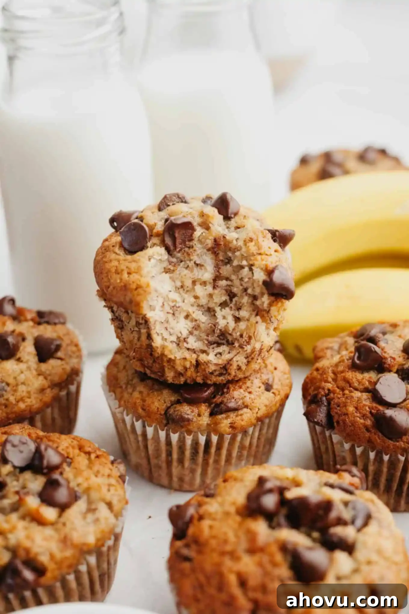 A stack of two banana chocolate chip muffins, one with a bite missing, showcasing their moist texture and generous chocolate chips.