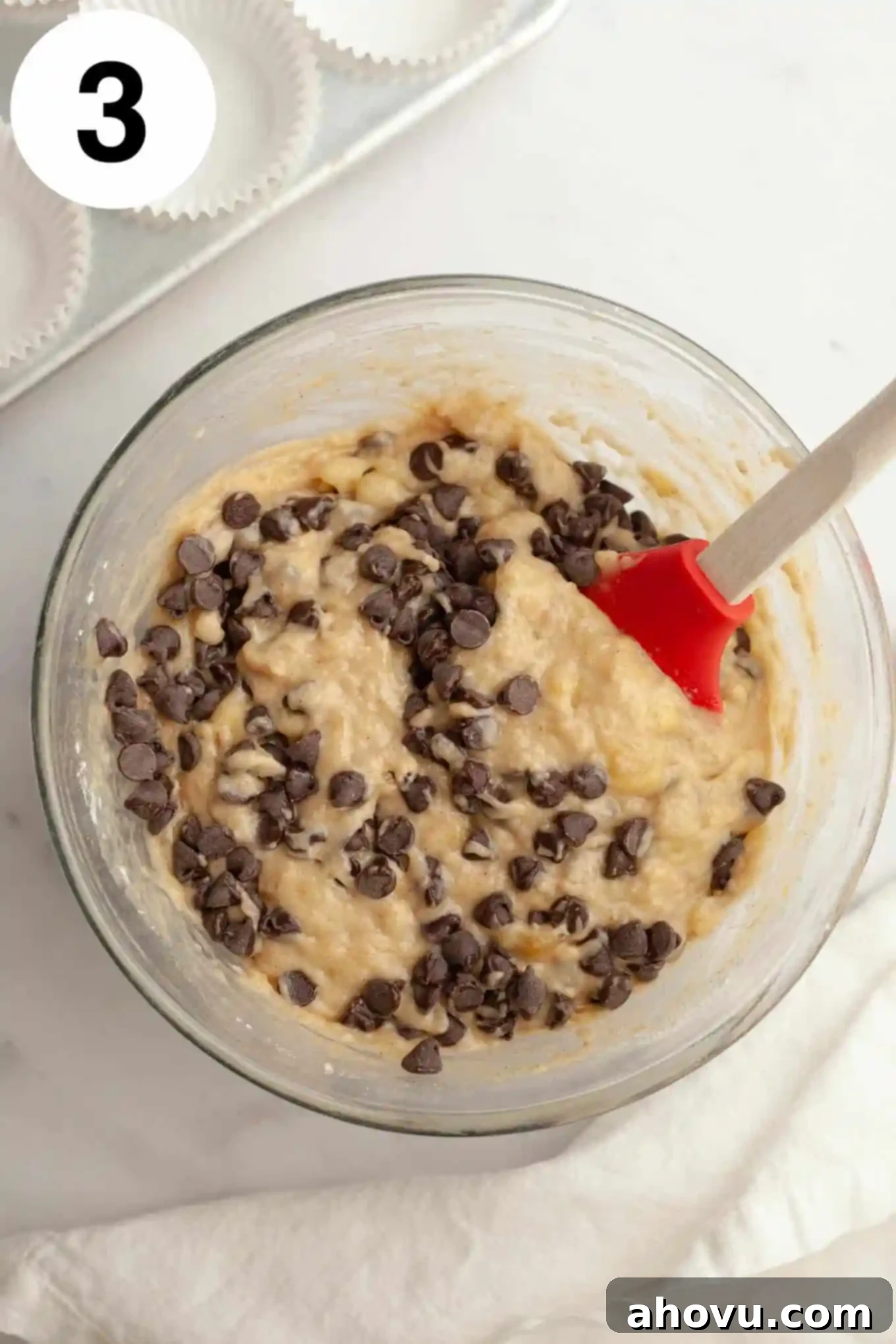 An overhead view of a banana chocolate chip muffin batter in a glass mixing bowl, showing the combined wet and dry ingredients before baking.