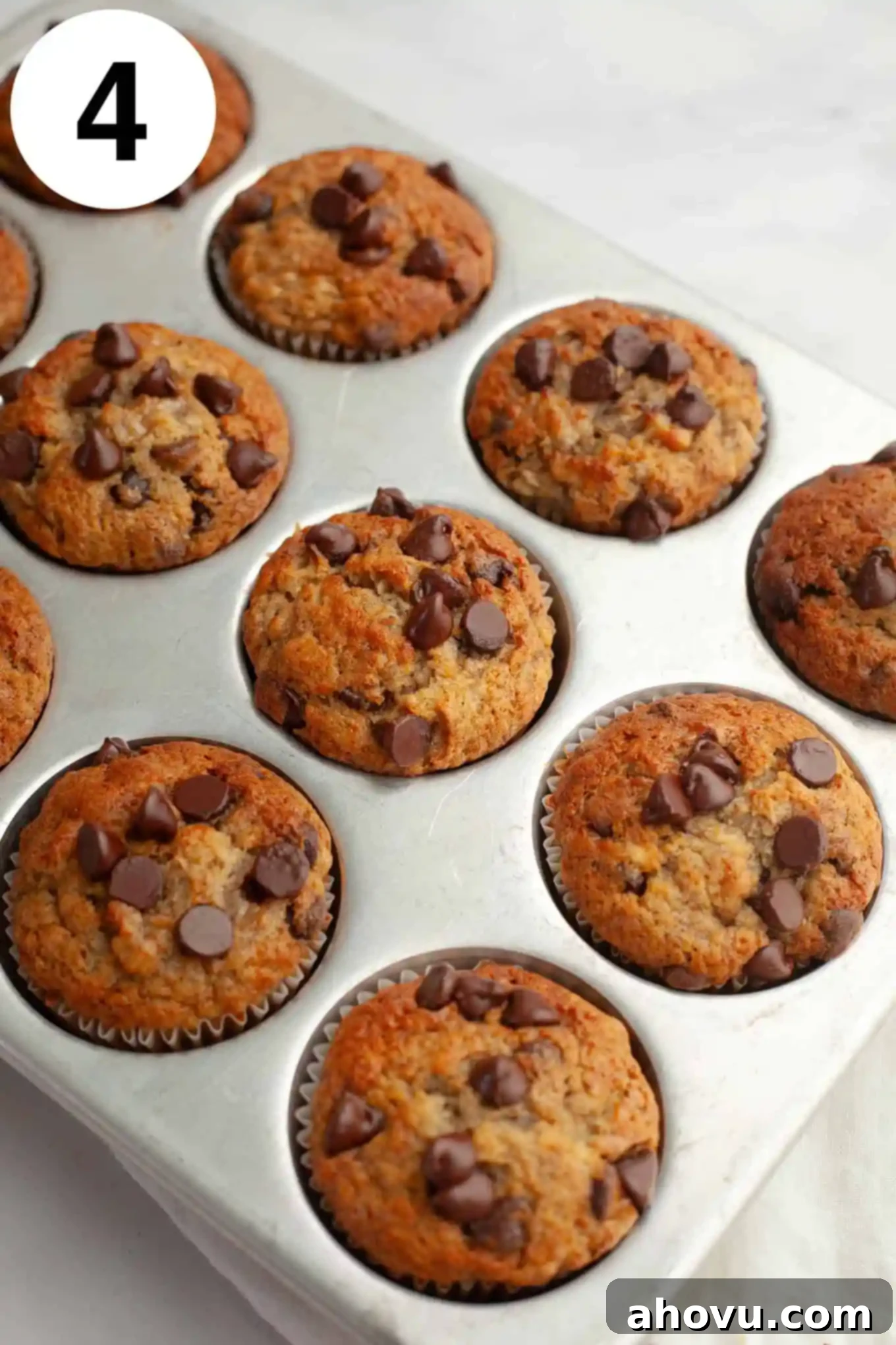 An overhead view of golden-brown baked banana muffins with glistening chocolate chips, resting in a muffin tray, fresh from the oven.