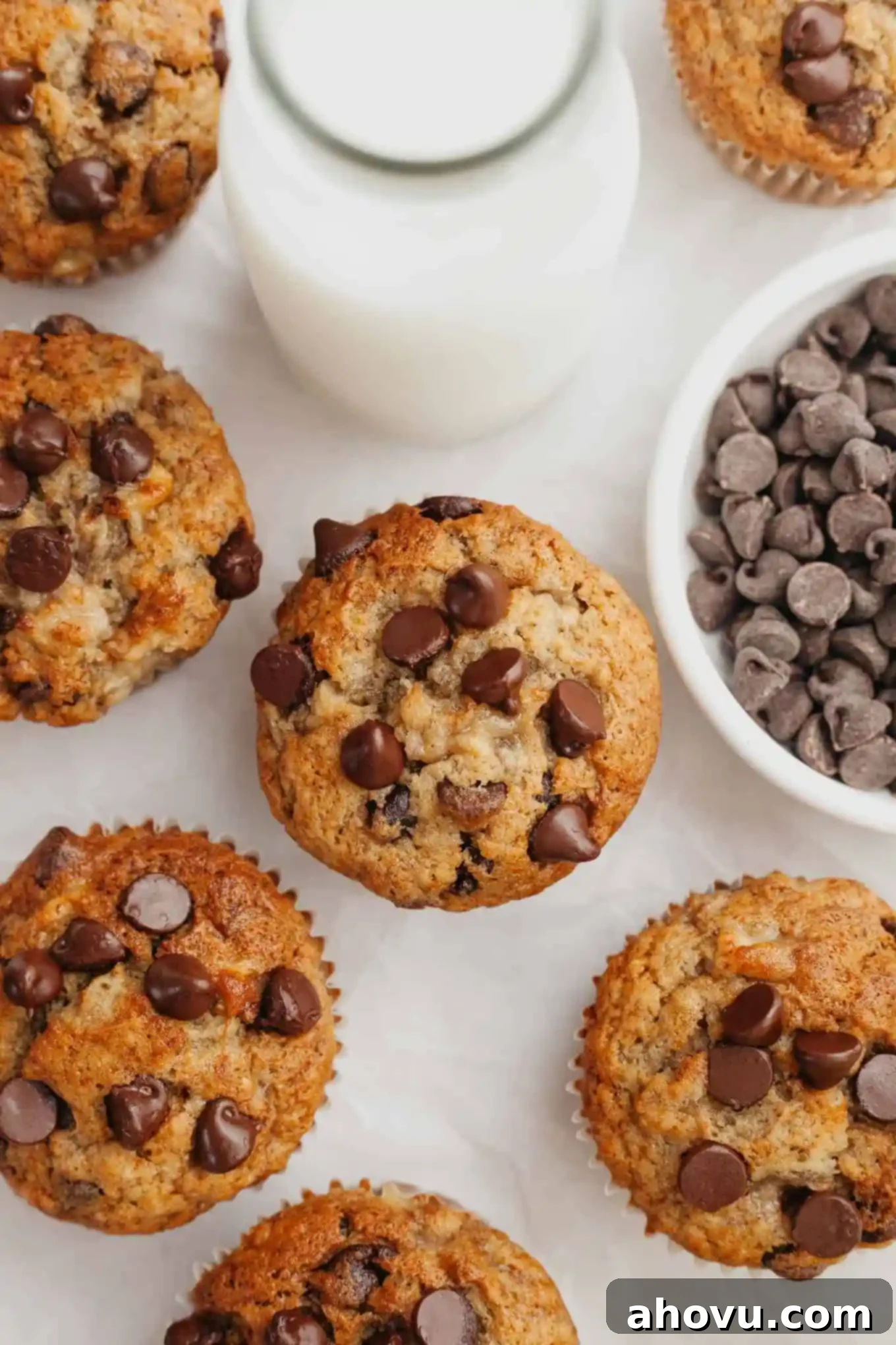 An overhead view of several golden-brown banana chocolate chip muffins cooling on a piece of white parchment paper, ready to be enjoyed.