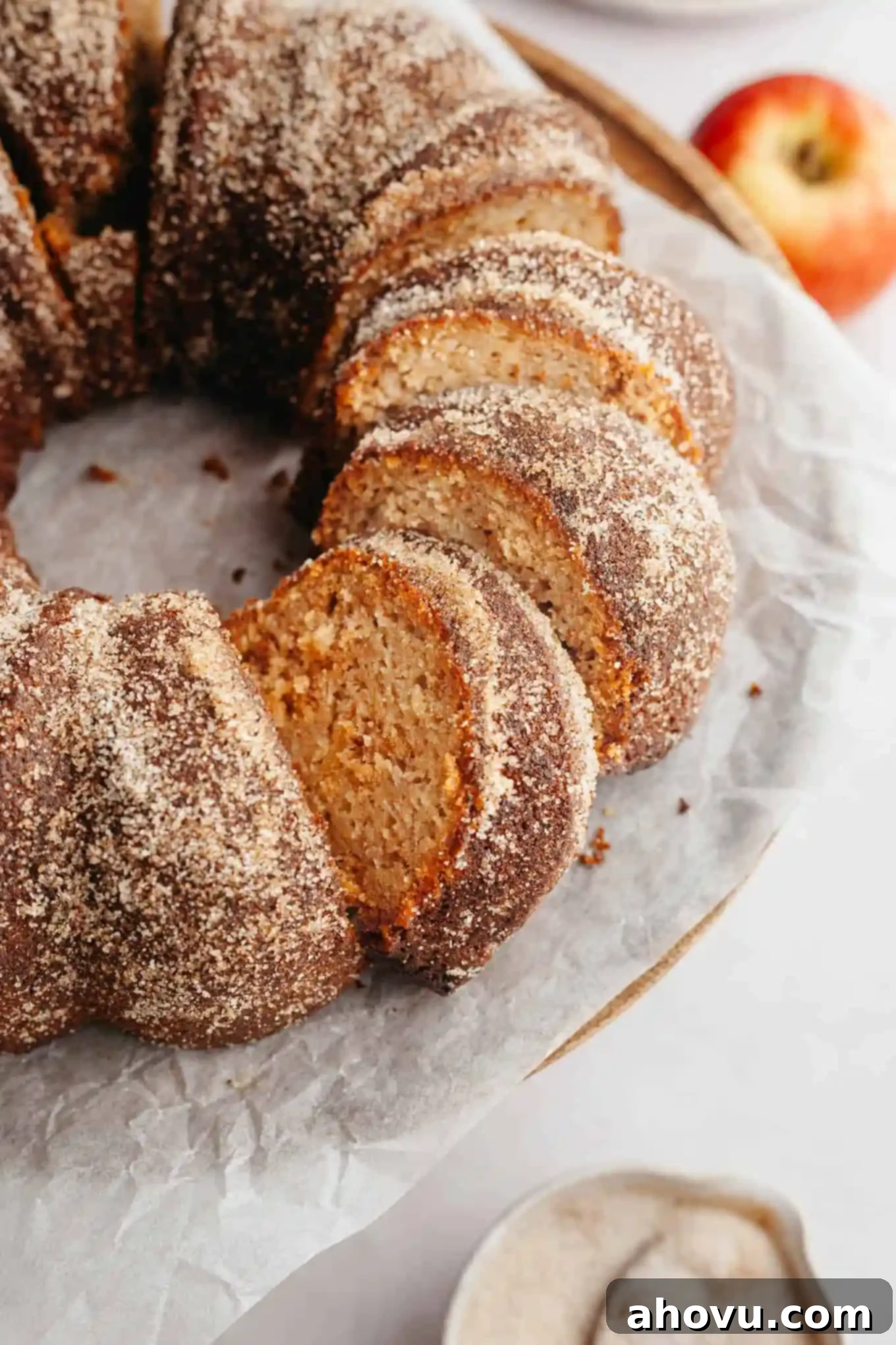 A beautifully sliced apple cider donut bundt cake on parchment paper, revealing its moist interior and cinnamon sugar coating.
