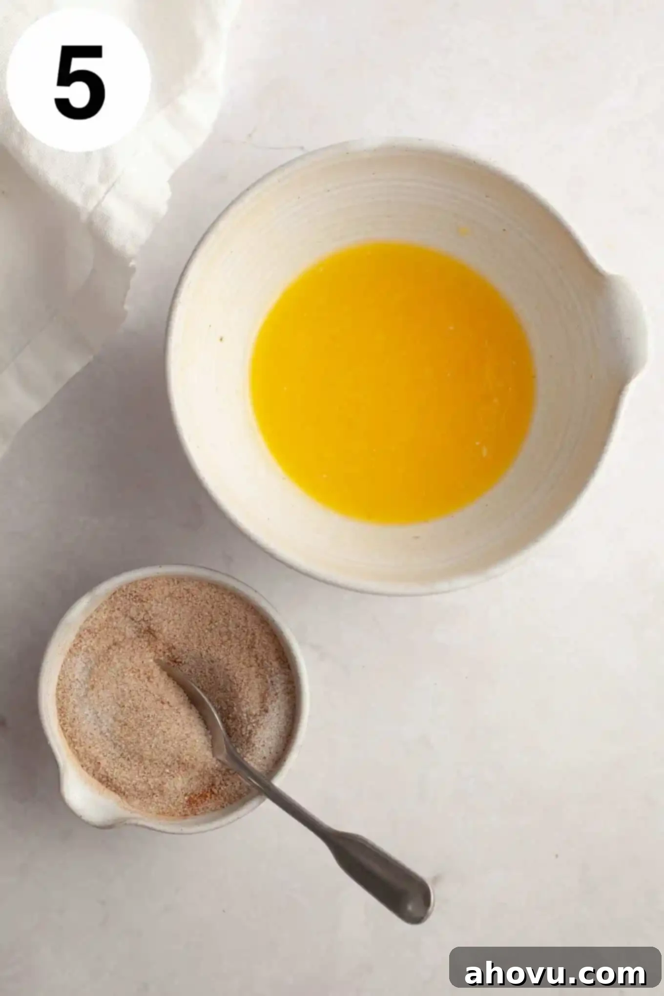 An overhead view of the melted butter and apple cider mixture in one bowl, and the cinnamon sugar blend in another, ready for the cake coating.