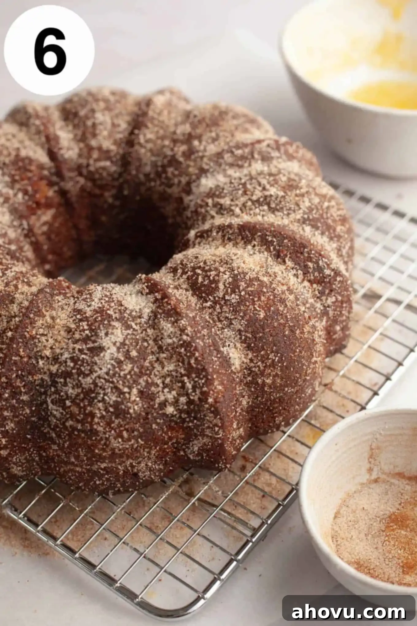 A freshly coated apple cider donut cake on a wire rack, glistening with cinnamon sugar.