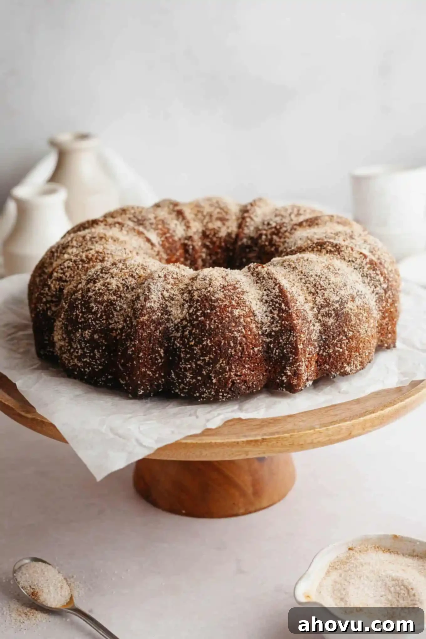 A beautifully cinnamon sugar-coated apple cider donut cake presented on a rustic wooden cake stand, ready to be enjoyed.