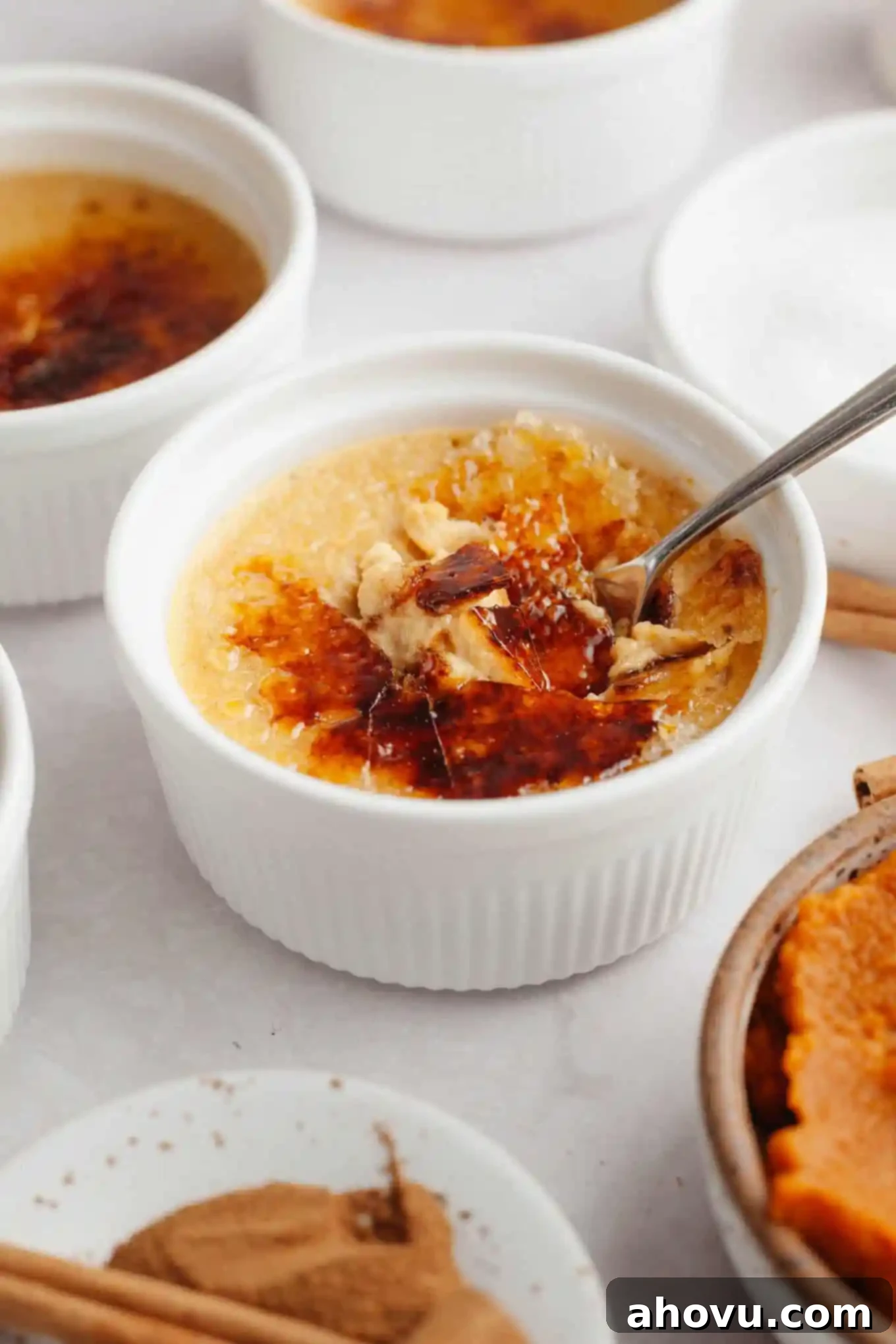 A ramekin of pumpkin crème brûlée with its crisp, caramelized sugar topping elegantly cracked open by a spoon, revealing the creamy custard inside.