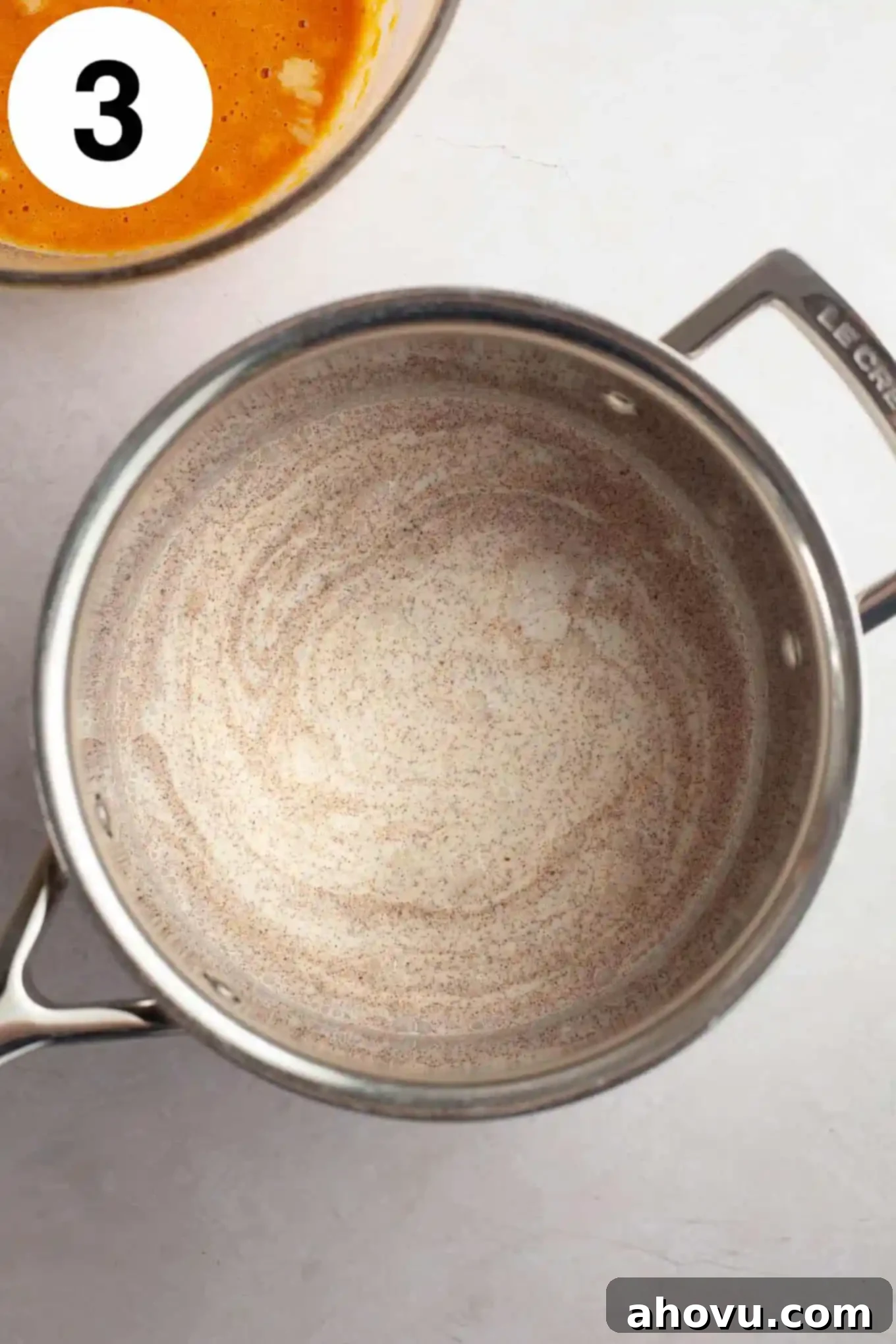 An overhead view of heavy cream and pumpkin pie spice warming in a saucepan on the stove.