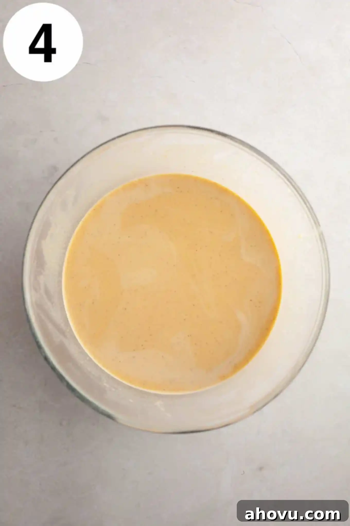 An overhead view of the creamy, raw pumpkin crème brûlée filling in a clear glass mixing bowl, ready for baking.