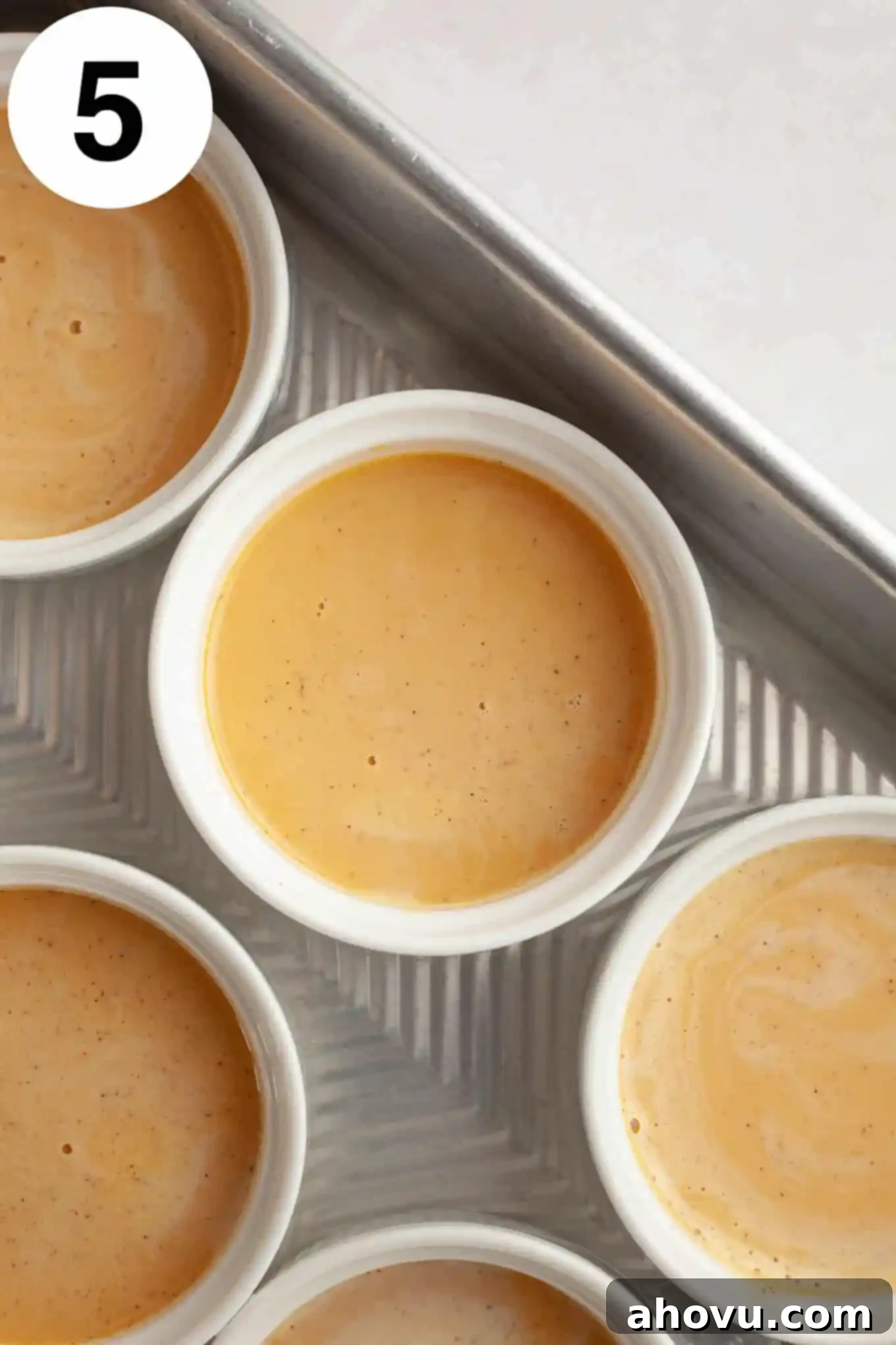 An overhead view of unbaked pumpkin crème brûlée custard in individual ramekins, placed in a water bath.