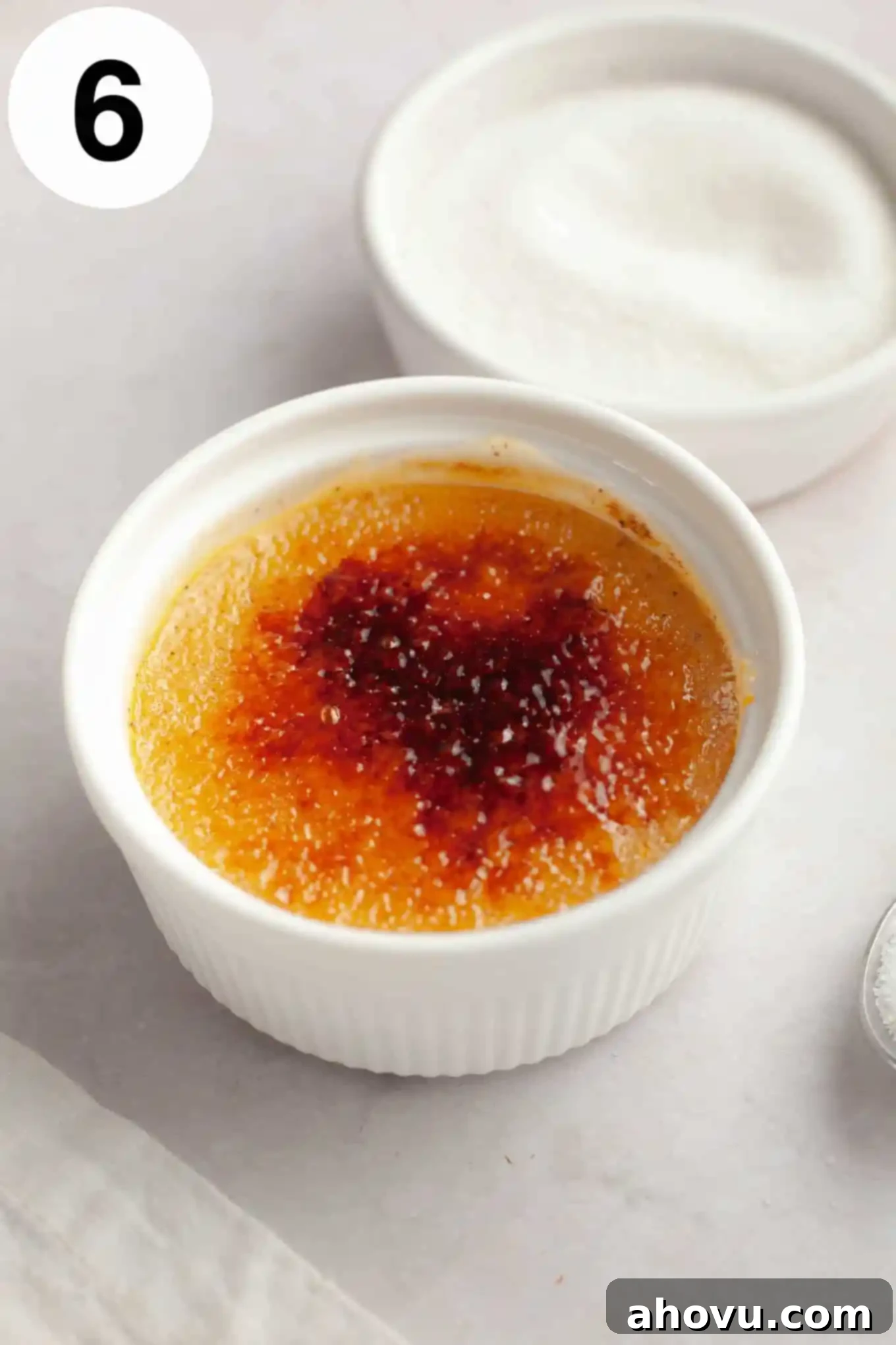 A single ramekin of unbaked pumpkin spice crème brûlée, with a small dish of granulated sugar beside it, ready for caramelization.