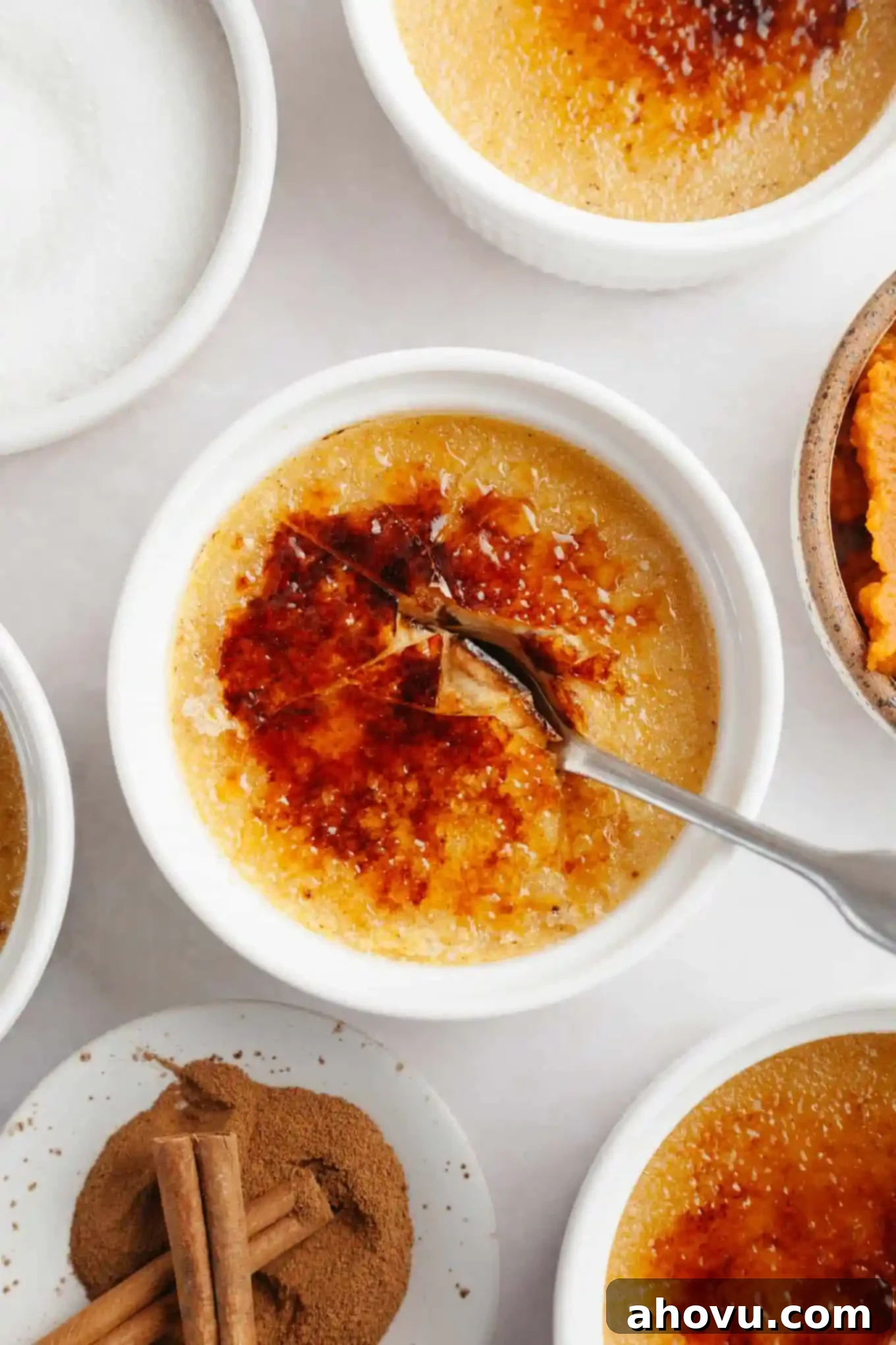 An overhead view of a spoon breaking through the crisp, caramelized topping of a pumpkin crème brûlée, revealing the creamy custard beneath.