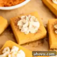 Several perfectly sliced pumpkin cheesecake bars, each featuring a gingersnap crust and creamy filling, arranged on a piece of brown parchment paper, ready to be served.