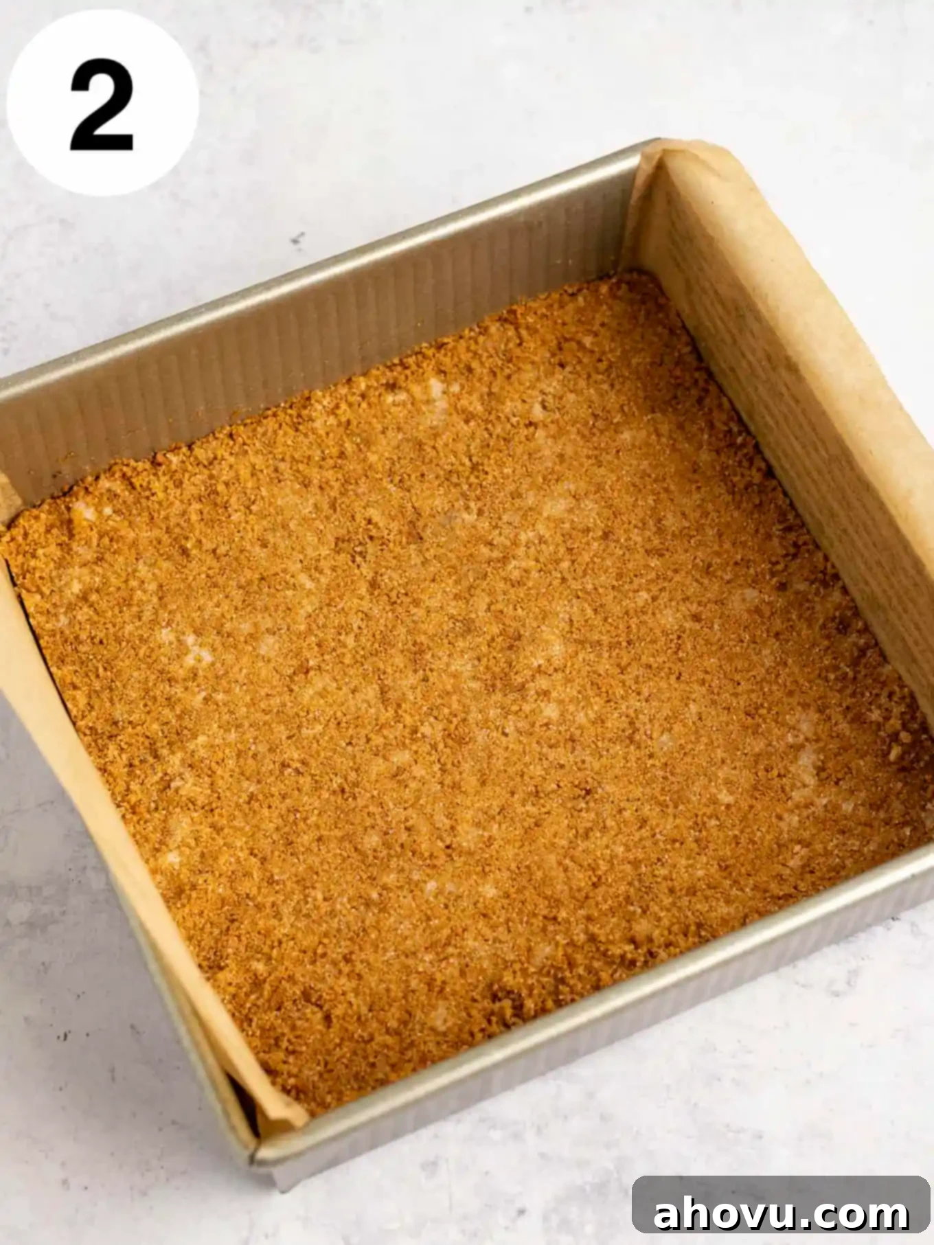 An overhead shot showcasing a golden-brown gingersnap crust, evenly pressed into a 9-inch square pan lined with parchment paper, ready for the filling.