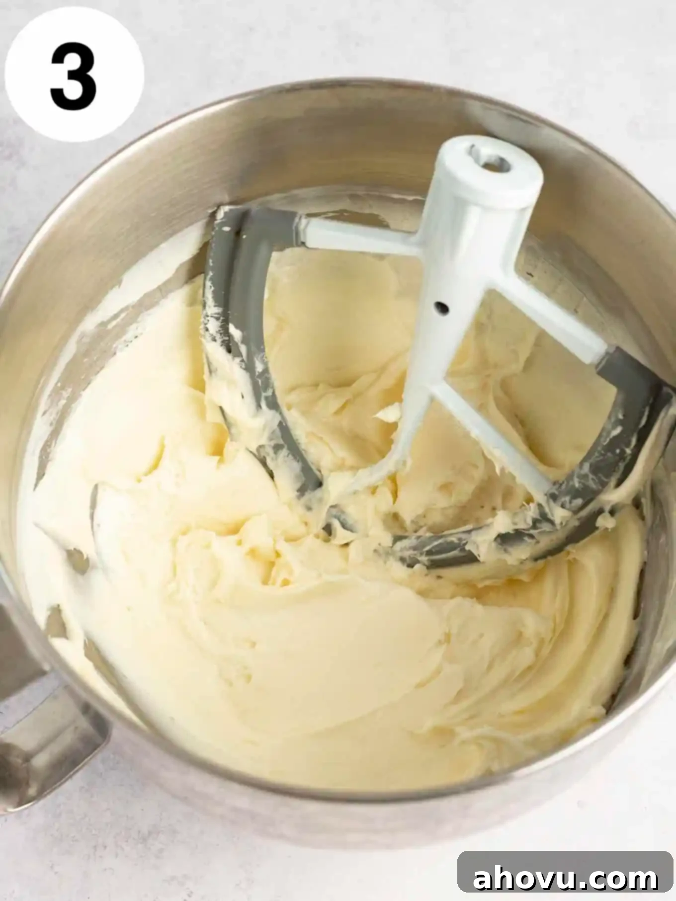 An overhead view of smooth, beaten cream cheese in the bowl of a stand mixer, demonstrating proper softening and mixing.