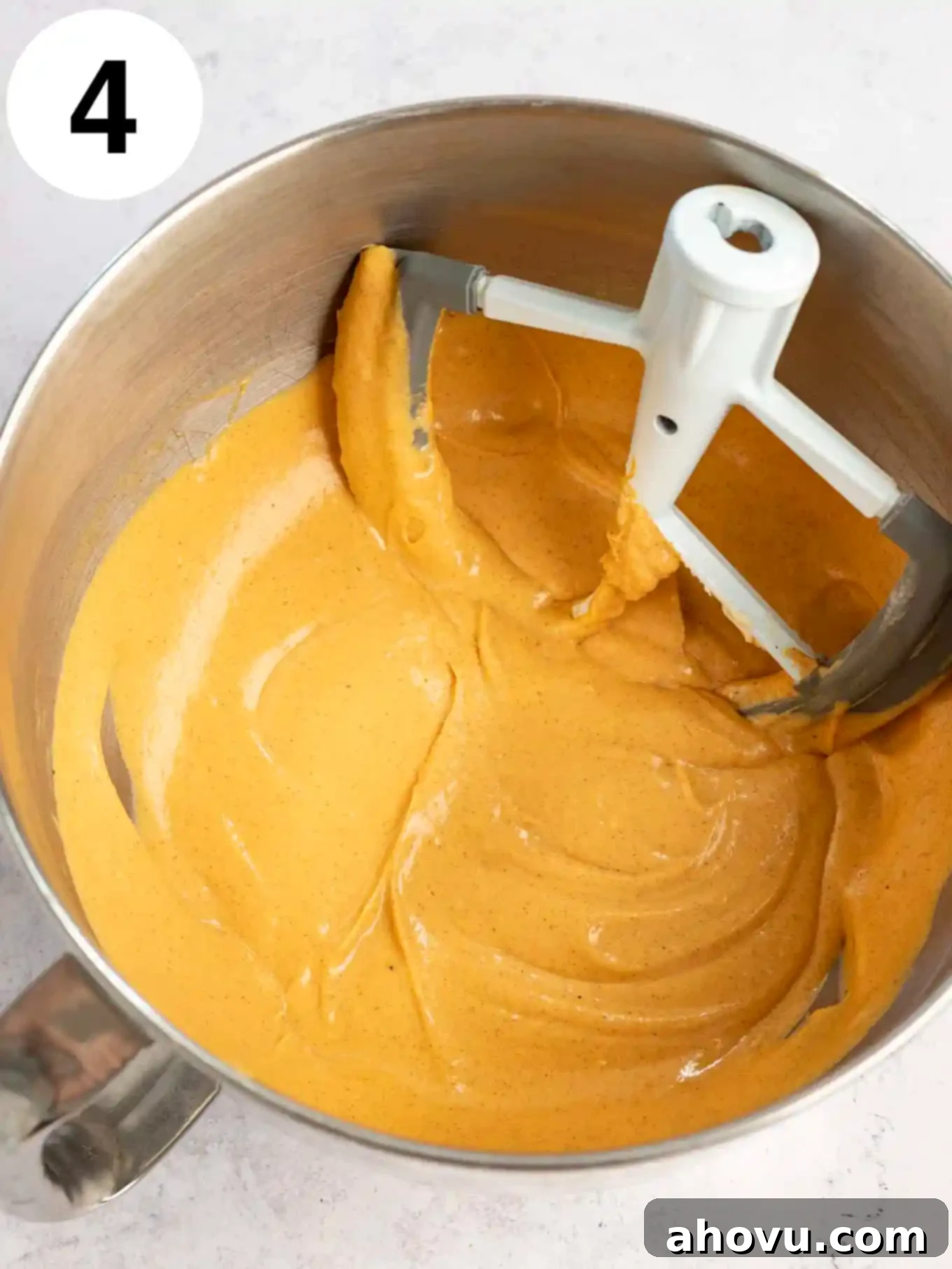 An overhead view of creamy pumpkin cheesecake filling in a stand mixer bowl, perfectly blended with a paddle attachment and ready for baking.