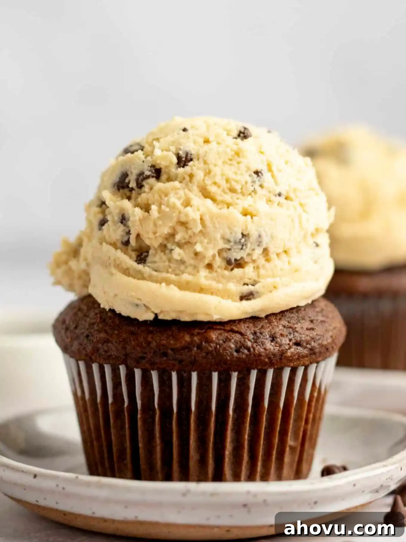 A perfectly frosted chocolate cupcake, topped with a generous scoop of creamy cookie dough frosting and adorned with mini chocolate chips.