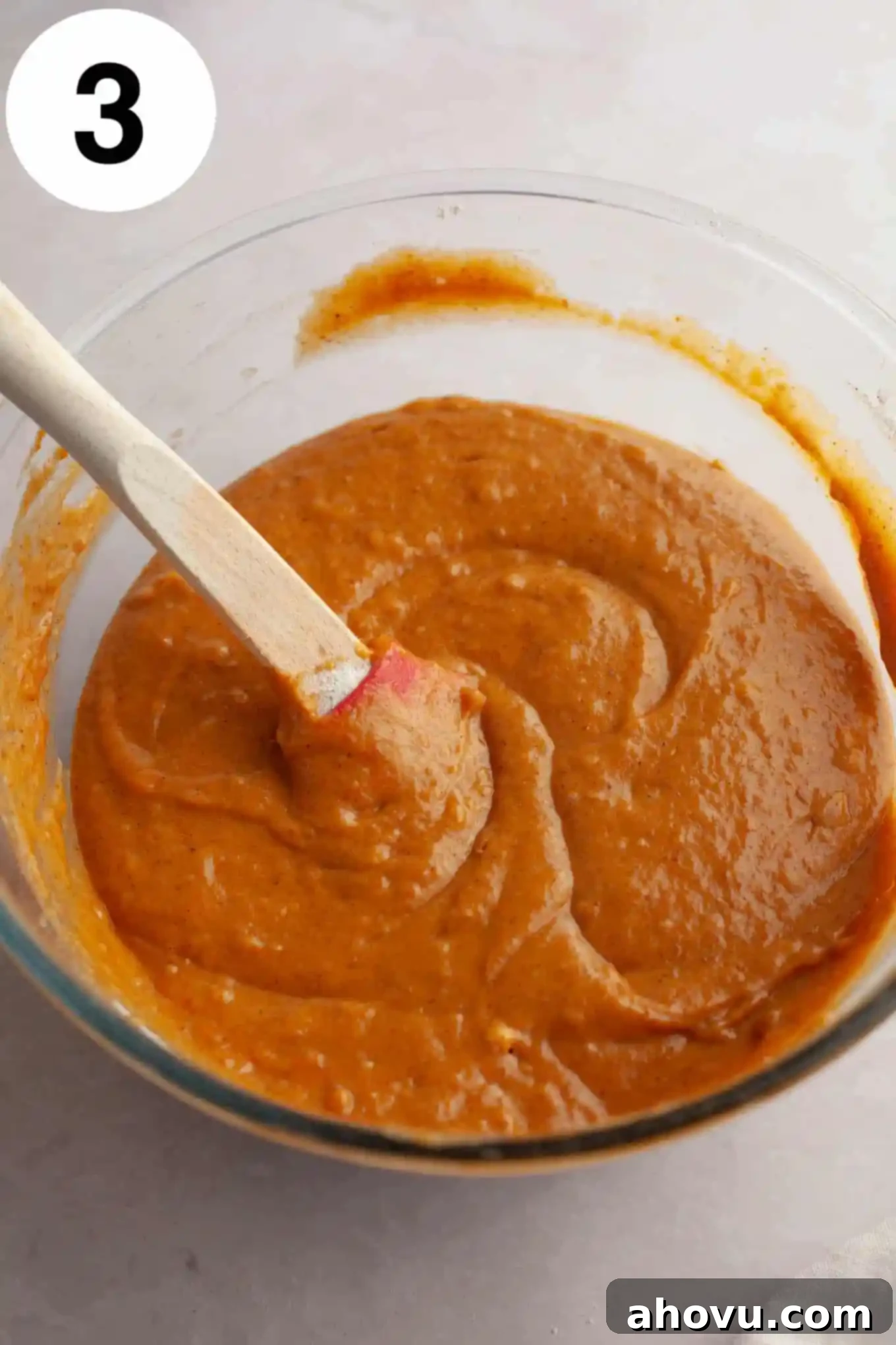 Pumpkin Swirl Cream Cheese Bread 6 An overhead view of a thick, orange pumpkin bread batter in a glass bowl, with a rubber spatula resting in it.