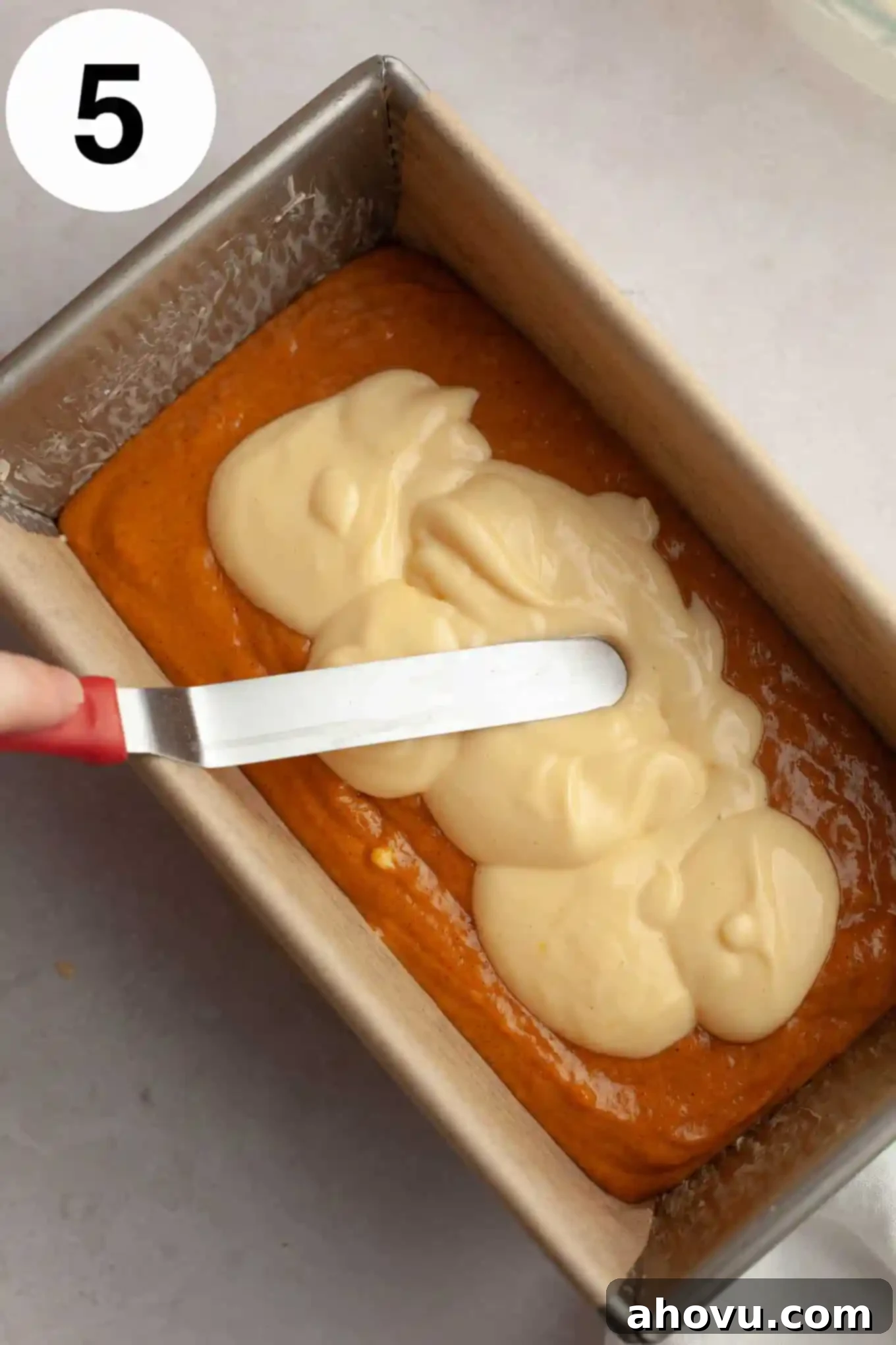 Pumpkin Swirl Cream Cheese Bread 8 An overhead view of a luscious cream cheese filling being carefully spread over a layer of pumpkin bread batter in a loaf pan, showing the layering process.