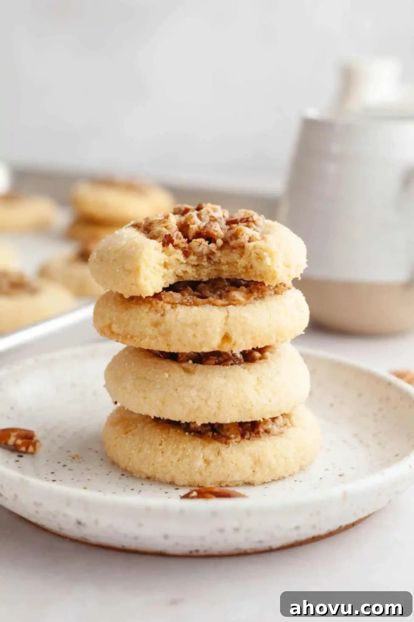 A stack of four pecan pie cookies, seen from the side. The top cookie has a bite missing, revealing the rich pecan filling and the golden brown shortbread base. 
