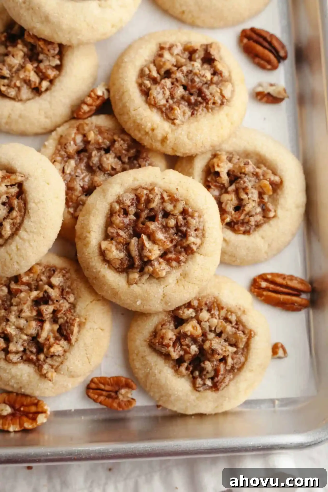 An overhead, close-up view of perfectly baked pecan pie cookies on a parchment paper-lined baking sheet, showcasing their golden edges and rich, bubbly filling. 