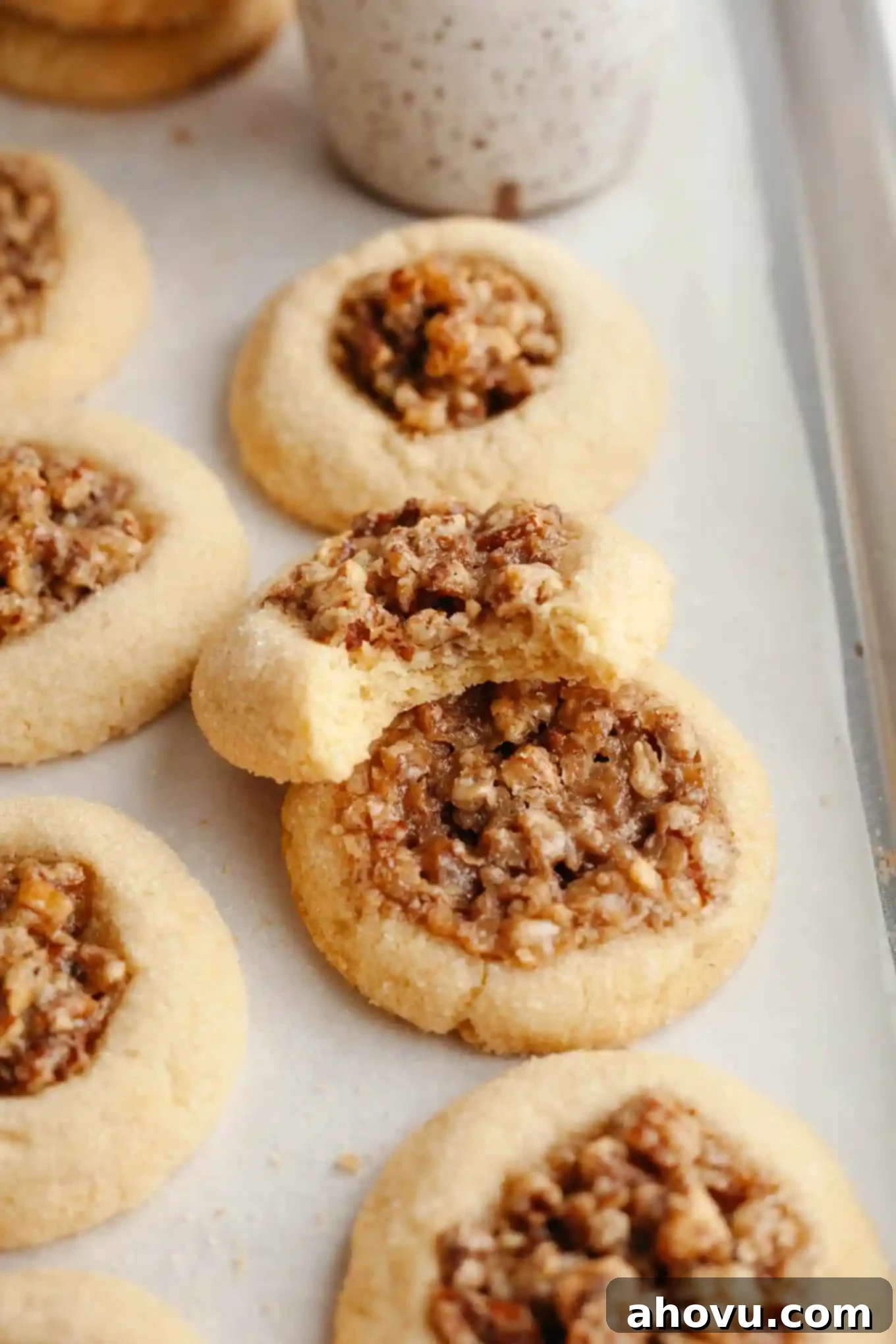 Pecan pie cookies arranged beautifully on a parchment-lined baking sheet. One cookie in the foreground has a bite missing, showcasing its delicious texture and filling. 