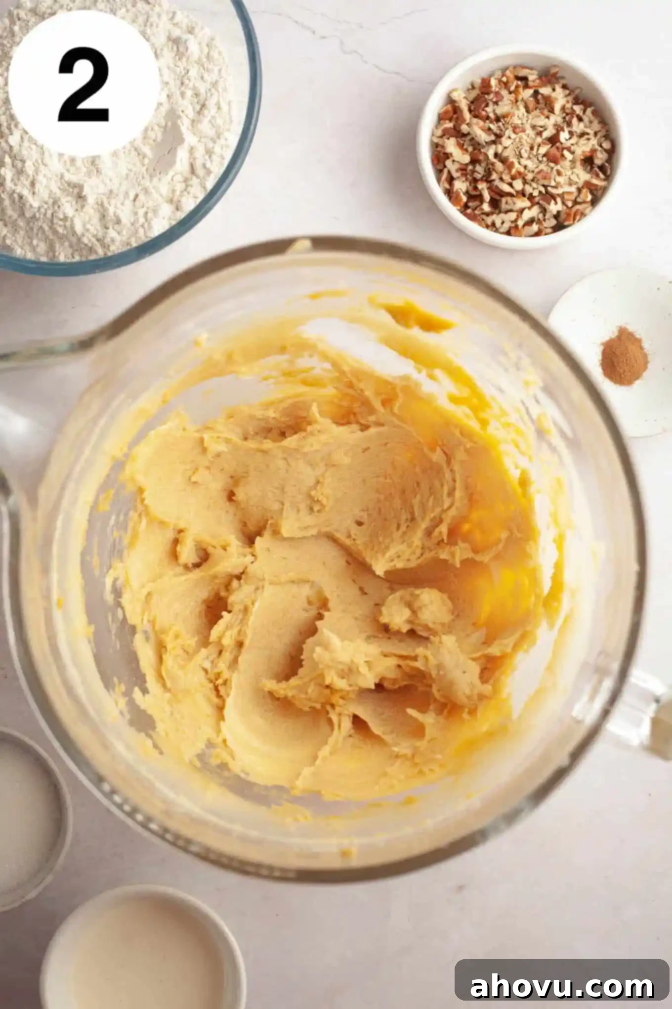 An overhead view of a wet cookie dough mixture, containing creamed butter, brown sugar, and egg yolks, in a glass mixing bowl, appearing smooth and well-incorporated. 