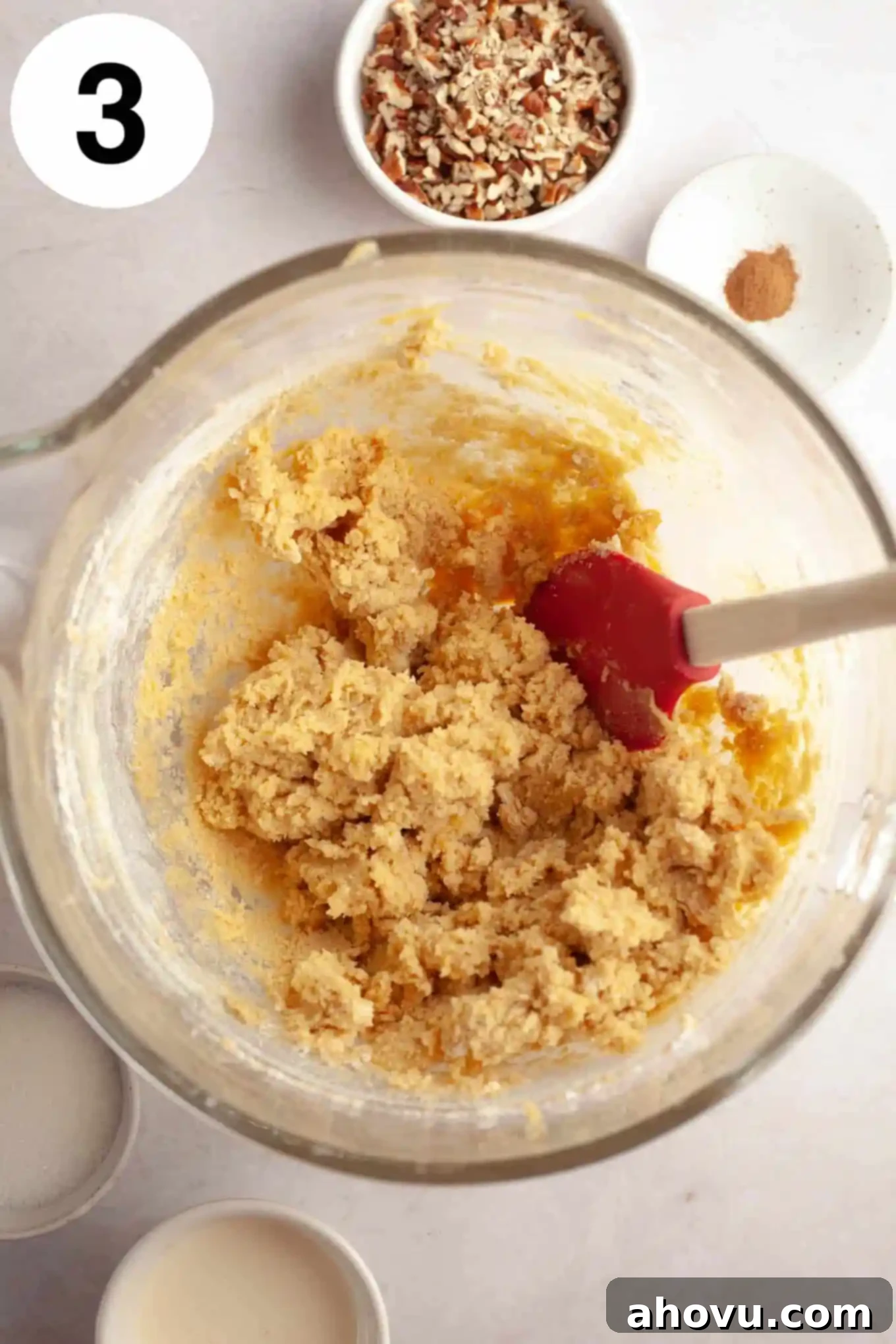 An overhead view of crumbly thumbprint cookie dough in a glass mixing bowl, ready to be pressed together. 