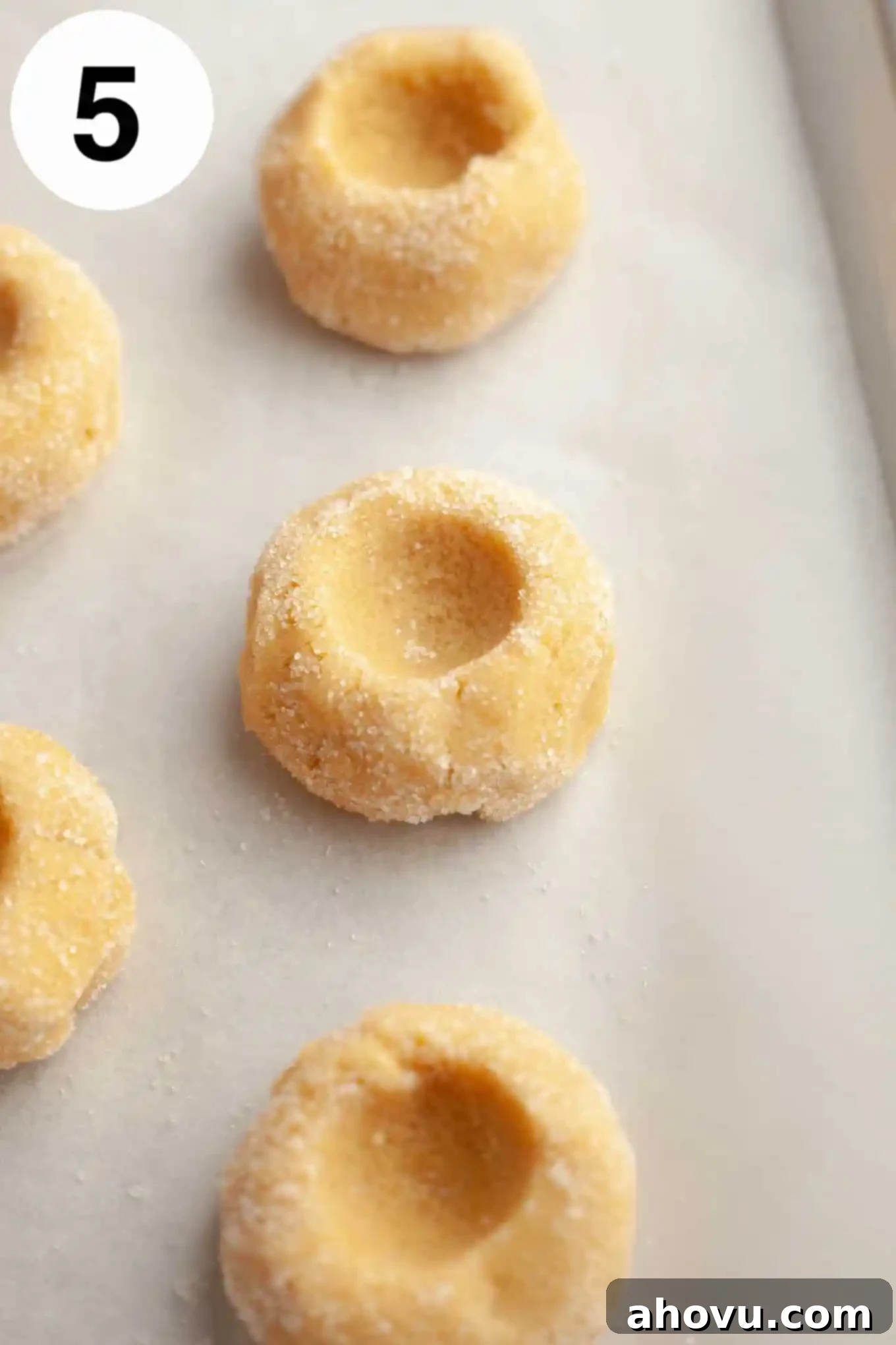 Raw, unfilled thumbprint cookies neatly arranged on a parchment paper-lined baking sheet, with visible indentations. 