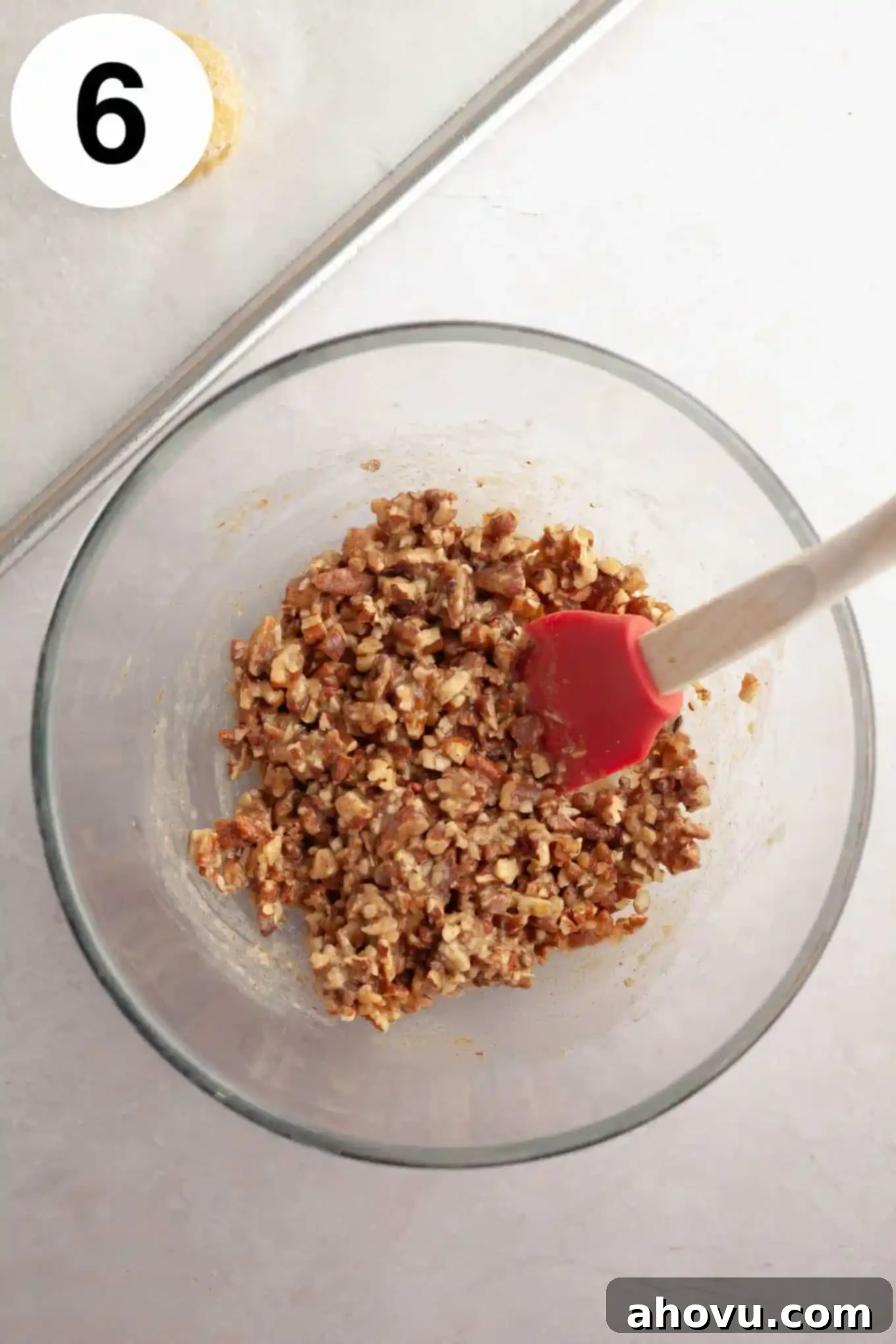 An overhead view of the pecan pie filling for cookies in a glass mixing bowl, showing chopped pecans, brown sugar, and cream mixed together. 