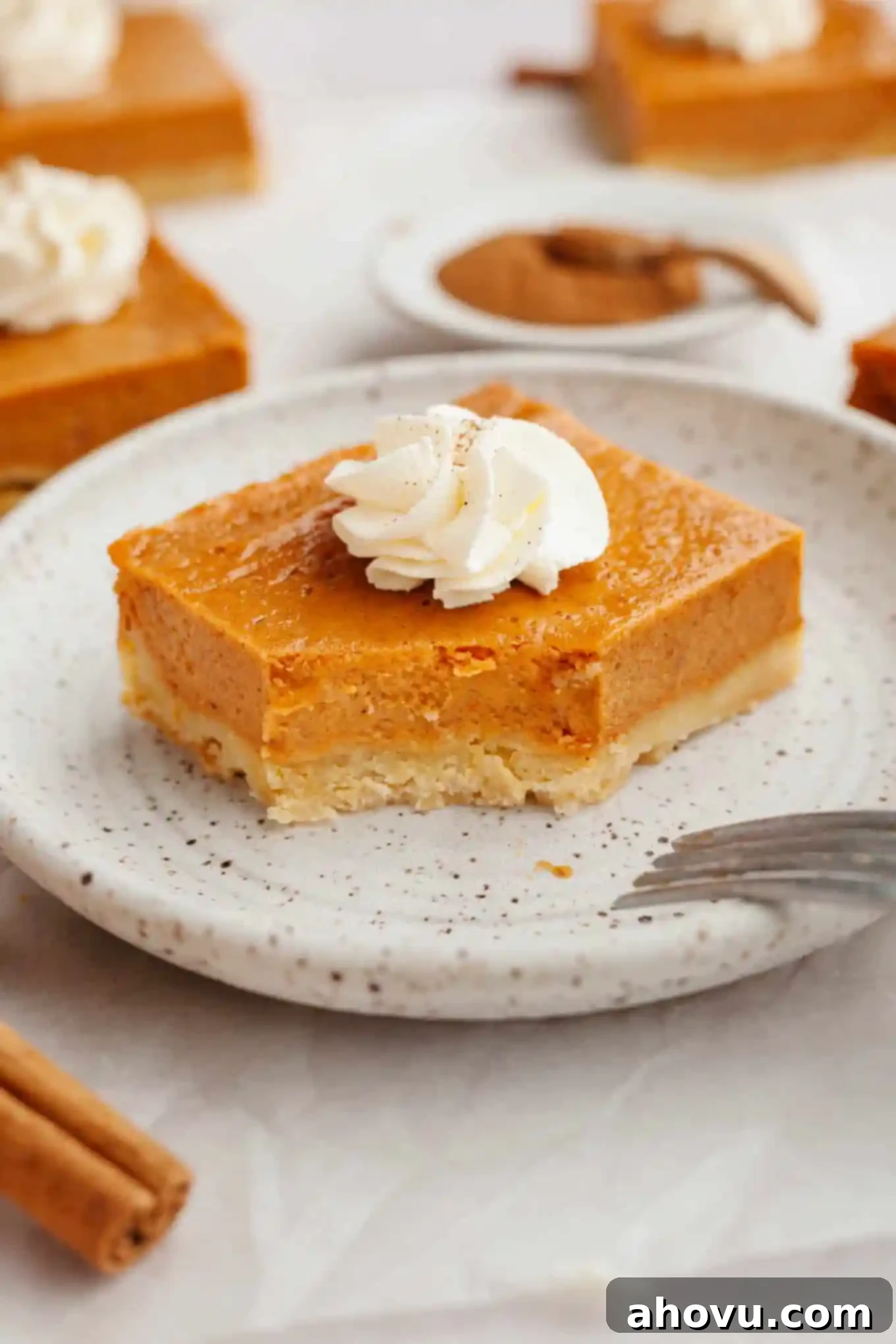 Harvest Spice Pumpkin Bars 11 A pumpkin pie bar garnished with whipped cream, on a dessert plate. A bite is missing.