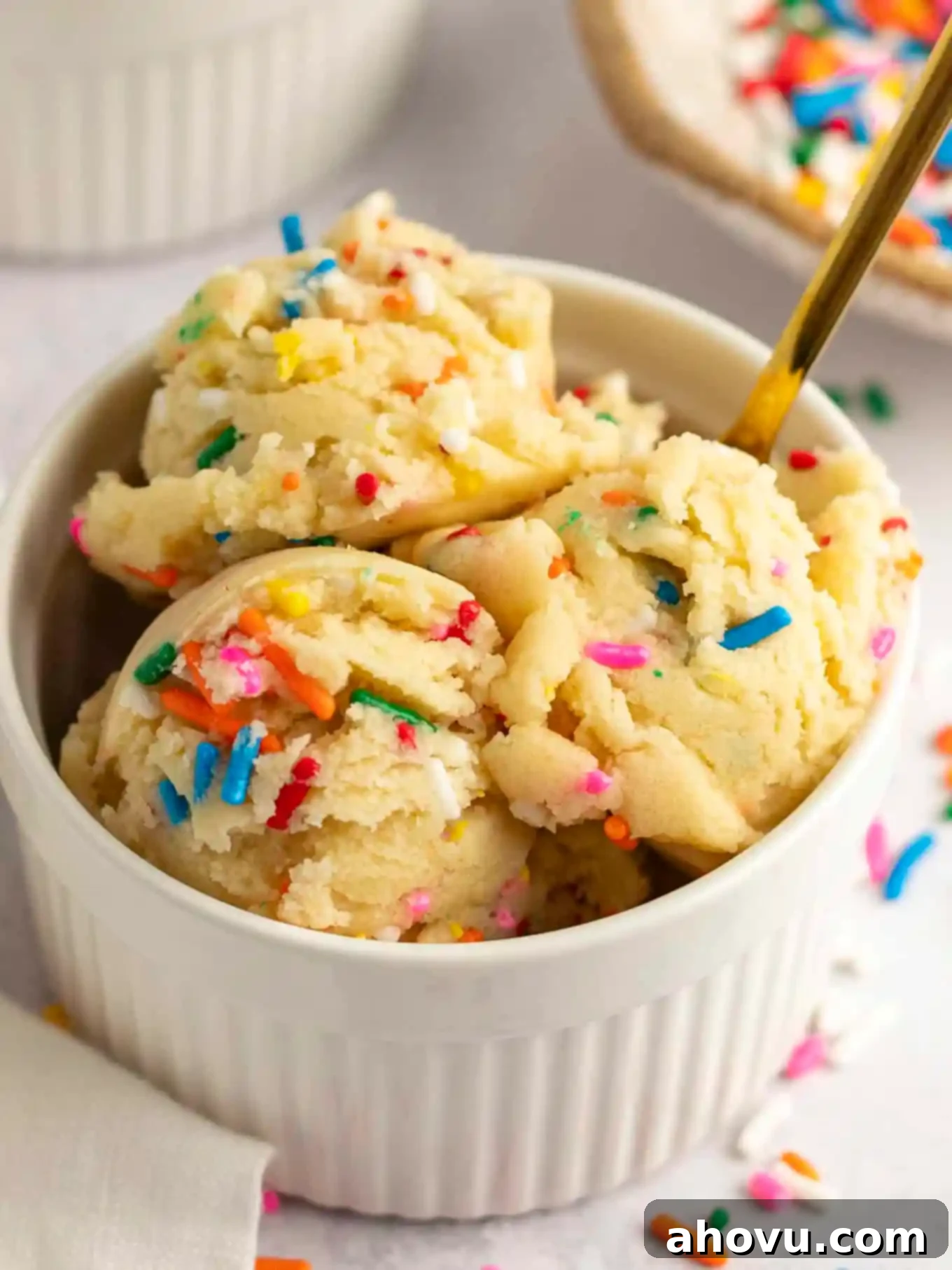 Guilt-Free Sugar Cookie Dough 11 A white ramekin filled with edible sugar cookie dough, beautifully garnished with colorful sprinkles, against a light background.