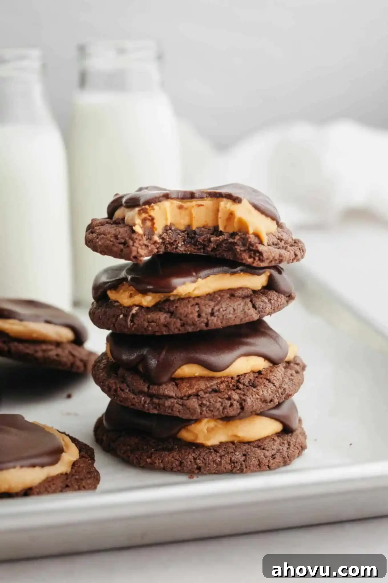 A stack of four Buckeye cookies; the top cookie is missing a bite. Each cookie features a dark chocolate base, a creamy peanut butter layer, and a delicate chocolate drizzle on top, showcasing the classic Buckeye candy appearance.
