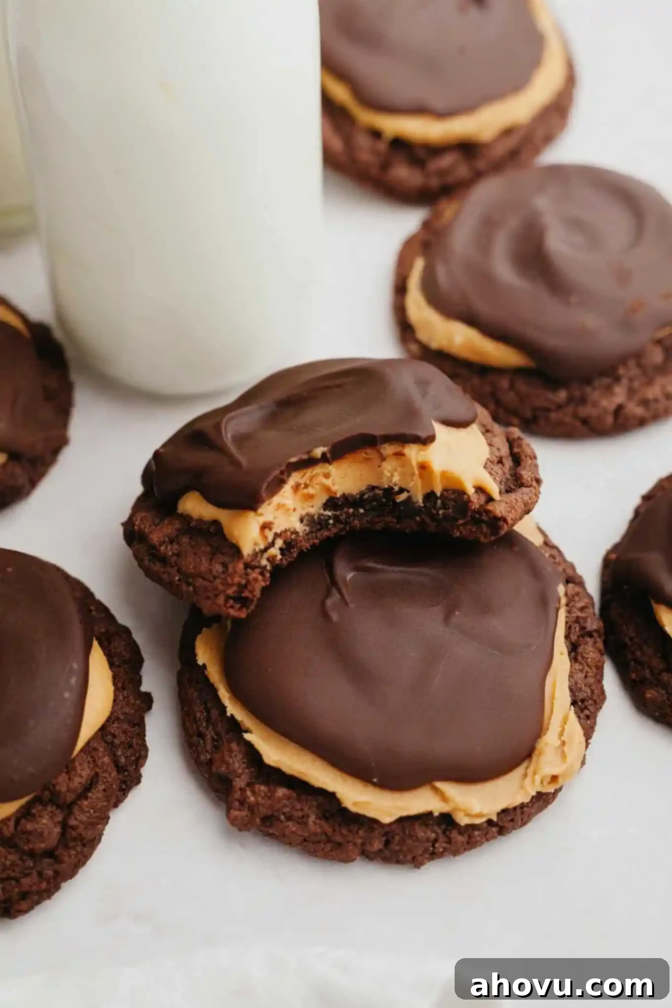 A close-up view of two finished Buckeye cookies, one with a bite taken out to reveal the layers of chocolate cookie, creamy peanut butter, and decadent chocolate topping.
