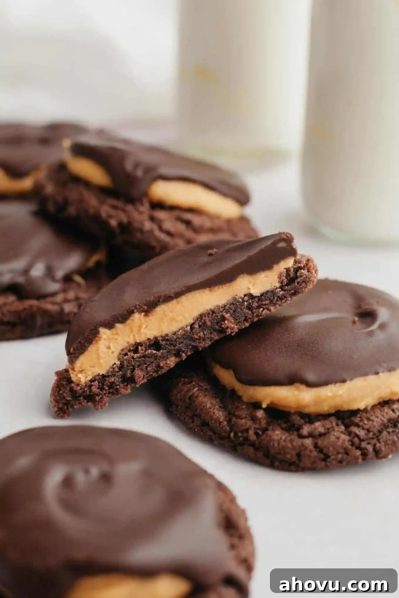Half of a delicious Buckeye cookie angled on top of another whole cookie, showcasing the distinct layers of chocolate cookie, peanut butter, and a chocolate drizzle. A bite has been taken from the half-cookie.