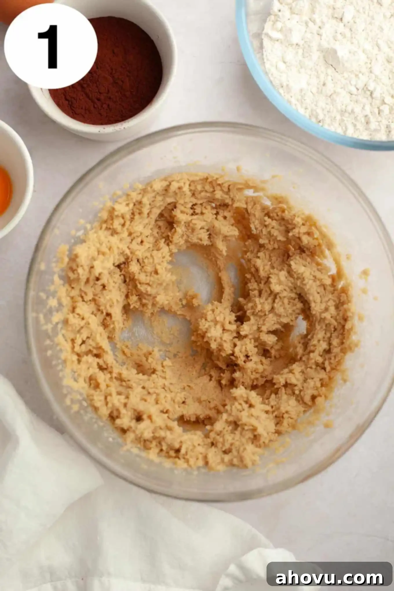 An overhead view of softened butter and light brown sugar being creamed together in a clear glass mixing bowl, a crucial first step in creating the chocolate cookie dough.