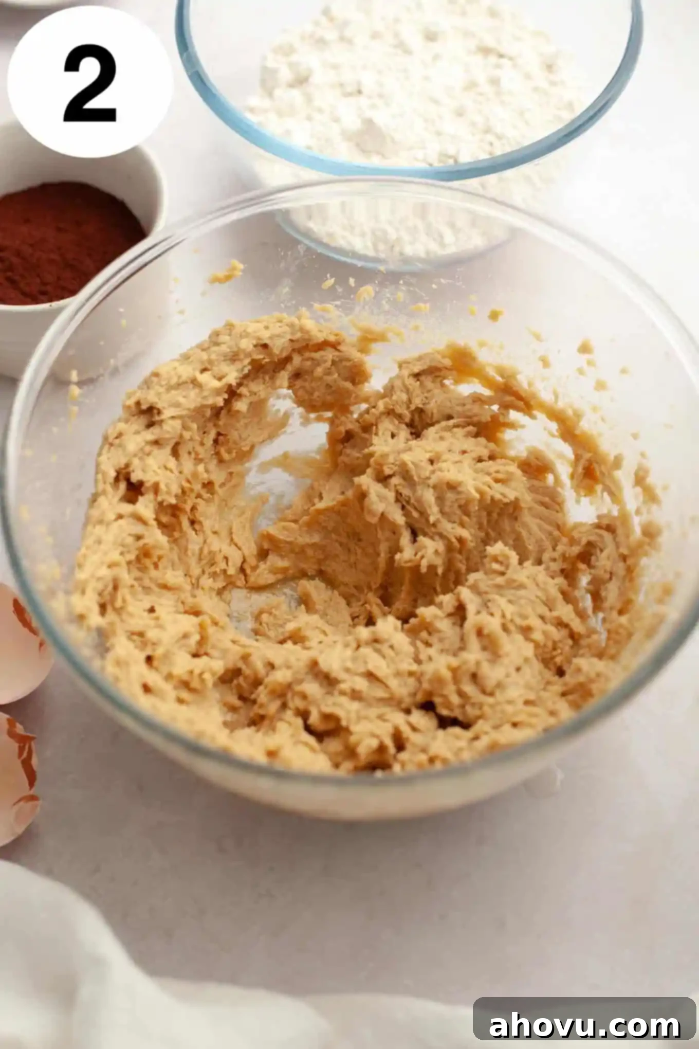 An overhead view of the wet ingredients for Buckeye cookies, including the creamed butter and sugars, along with eggs and vanilla extract, thoroughly mixed in a glass mixing bowl.