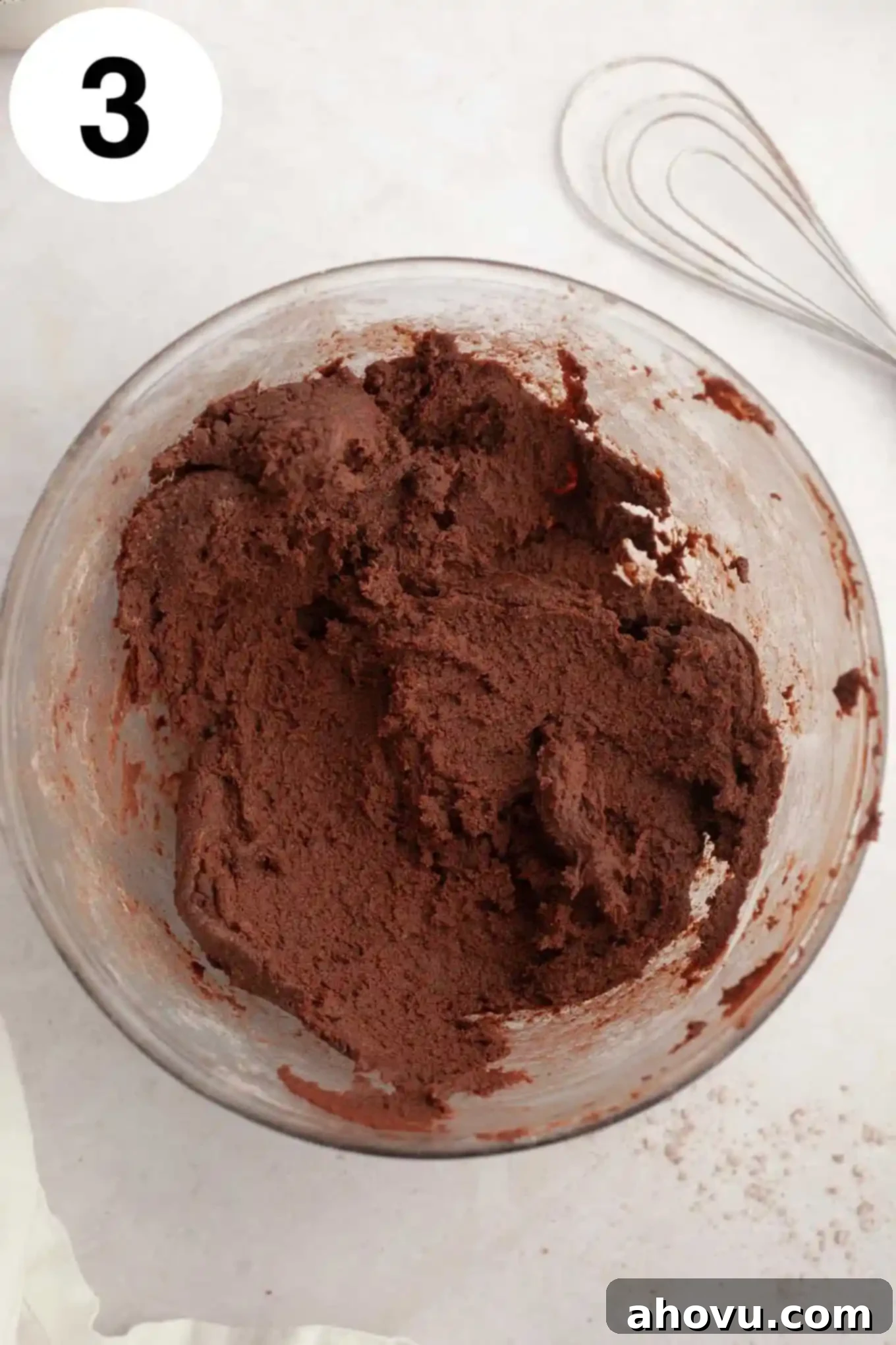 An overhead view of rich, dark chocolate cookie dough, perfectly mixed and ready for chilling, resting in a clear glass mixing bowl.