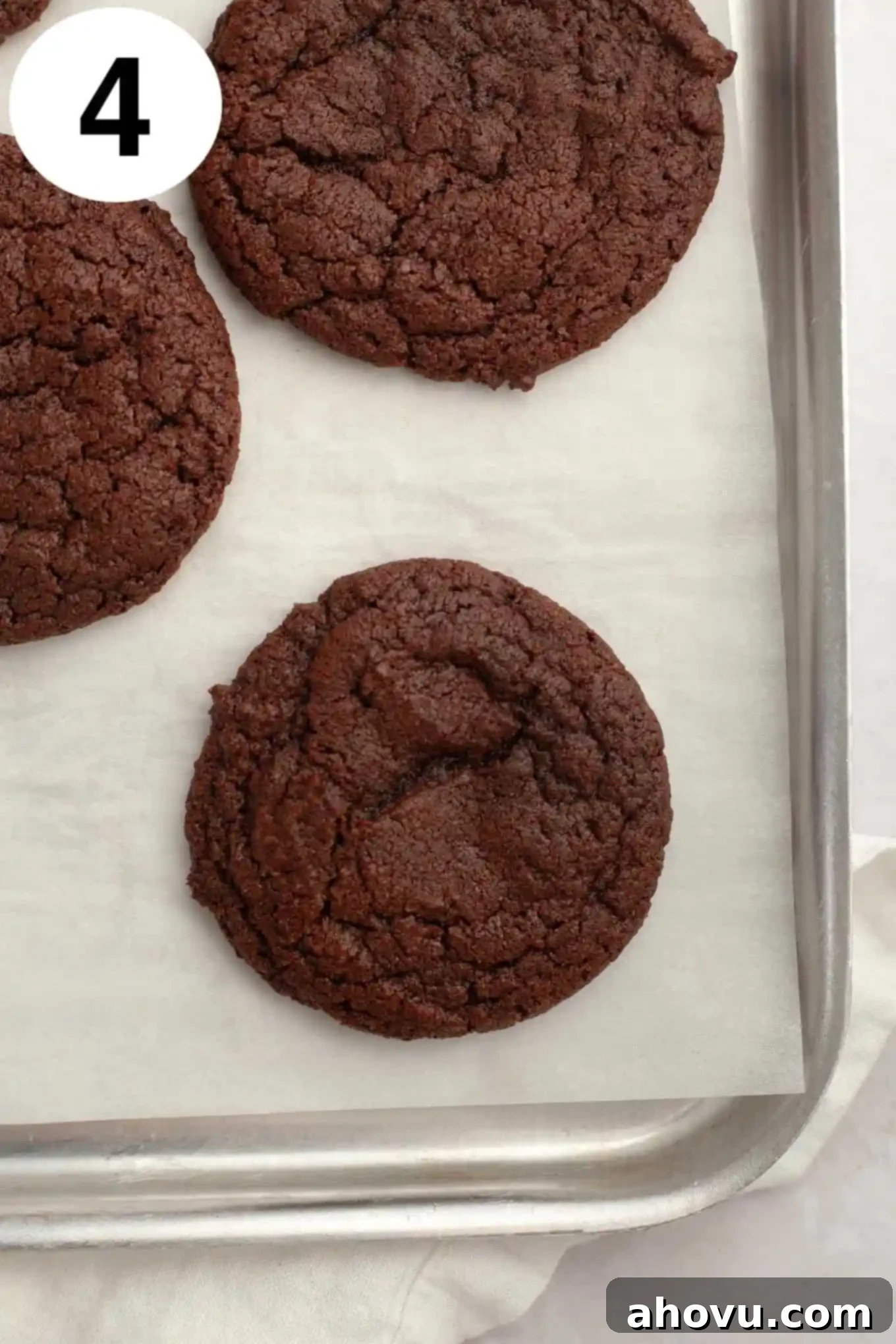 An overhead view of freshly baked, soft chocolate cookies cooling on a parchment-lined baking sheet, their tops set and ready for the next delicious layers.