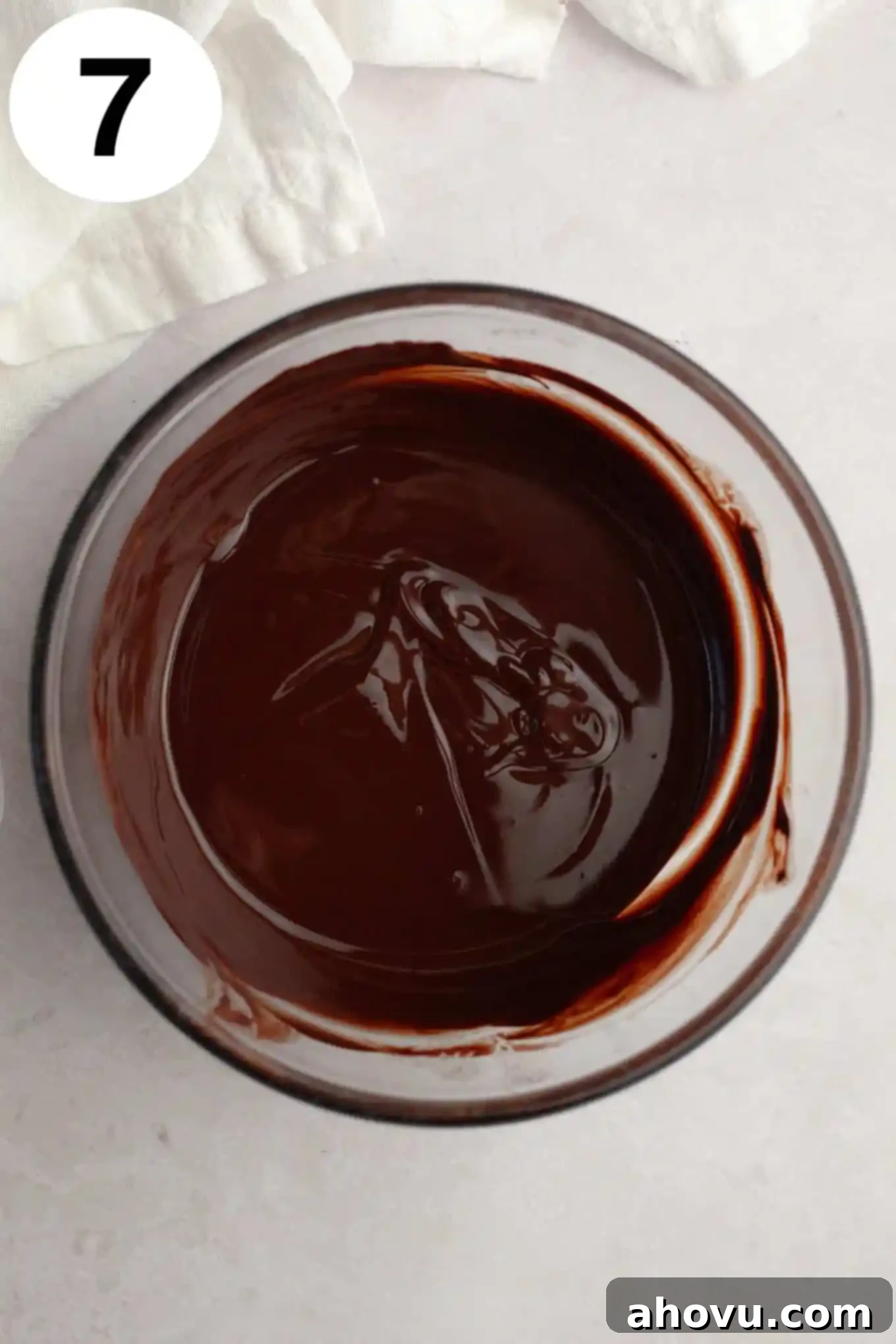 An overhead view of glossy, melted semi-sweet chocolate in a clear glass bowl, ready to be drizzled over the peanut butter-topped Buckeye cookies.