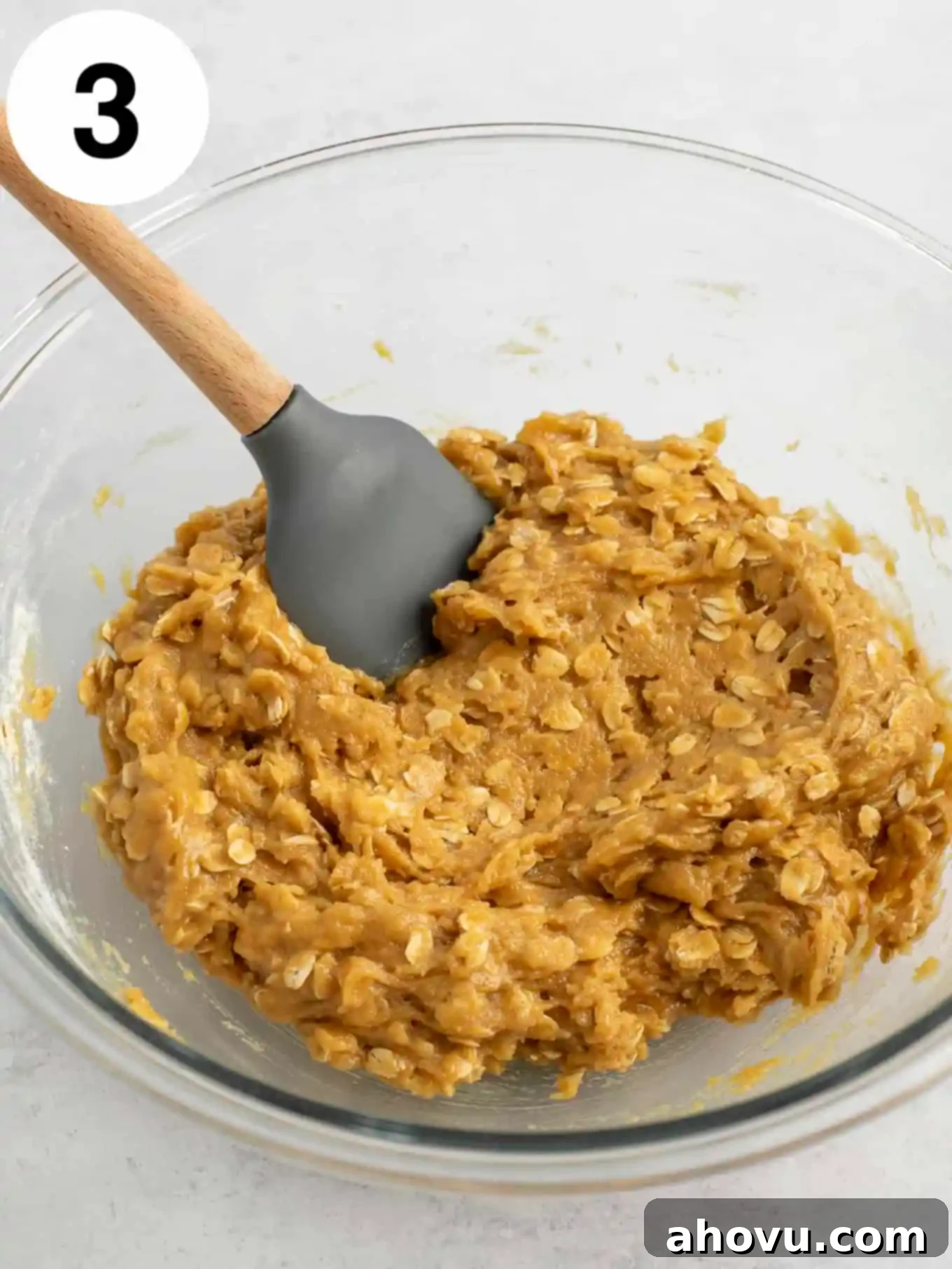 Peanut butter oatmeal cookie dough in a glass mixing bowl with a rubber spatula. 