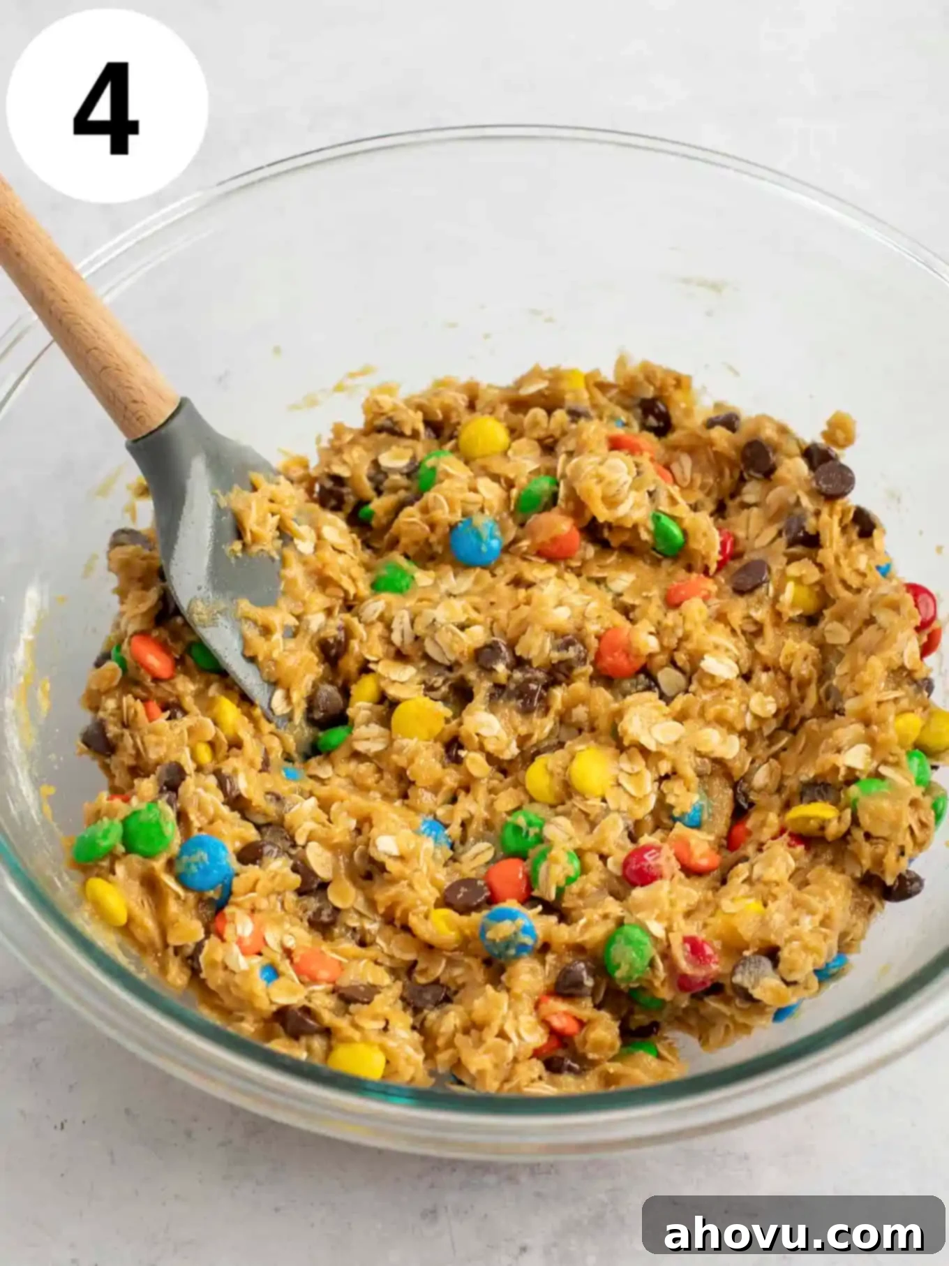 Monster cookie dough in a glass mixing bowl with a rubber spatula. 