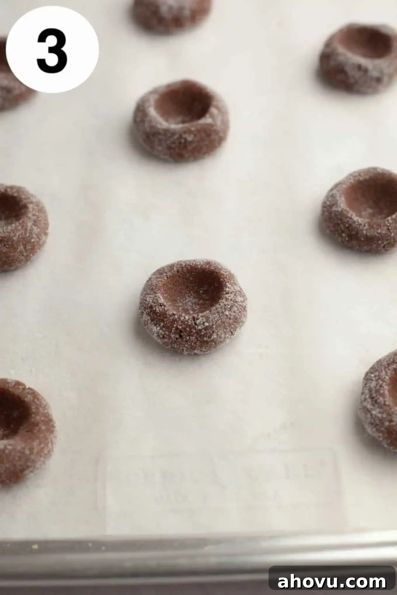 Irresistible Chocolate Thumbprint Cookies 6 Unbaked and unfilled chocolate thumbprints on a parchment lined baking sheet.