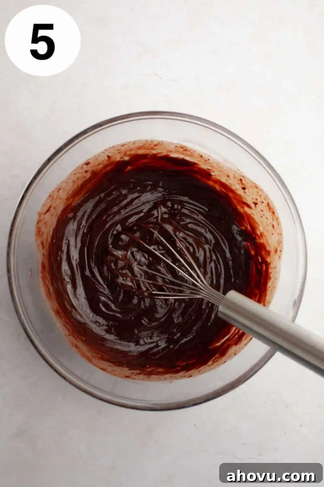 Irresistible Chocolate Thumbprint Cookies 8 An overhead view of melted chocolate ganache in a glass mixing bowl, with a whisk.
