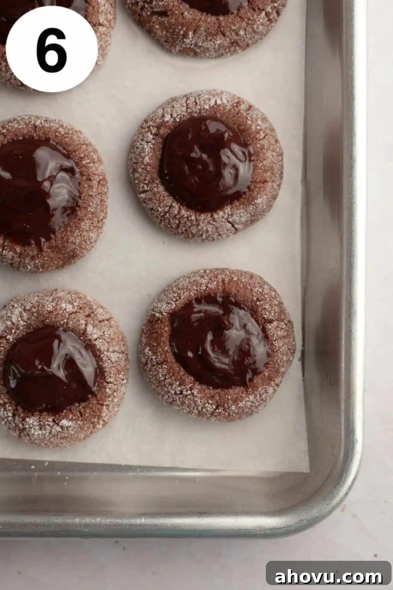 Irresistible Chocolate Thumbprint Cookies 9 An overhead view of filled chocolate thumbprints on a parchment lined baking sheet.
