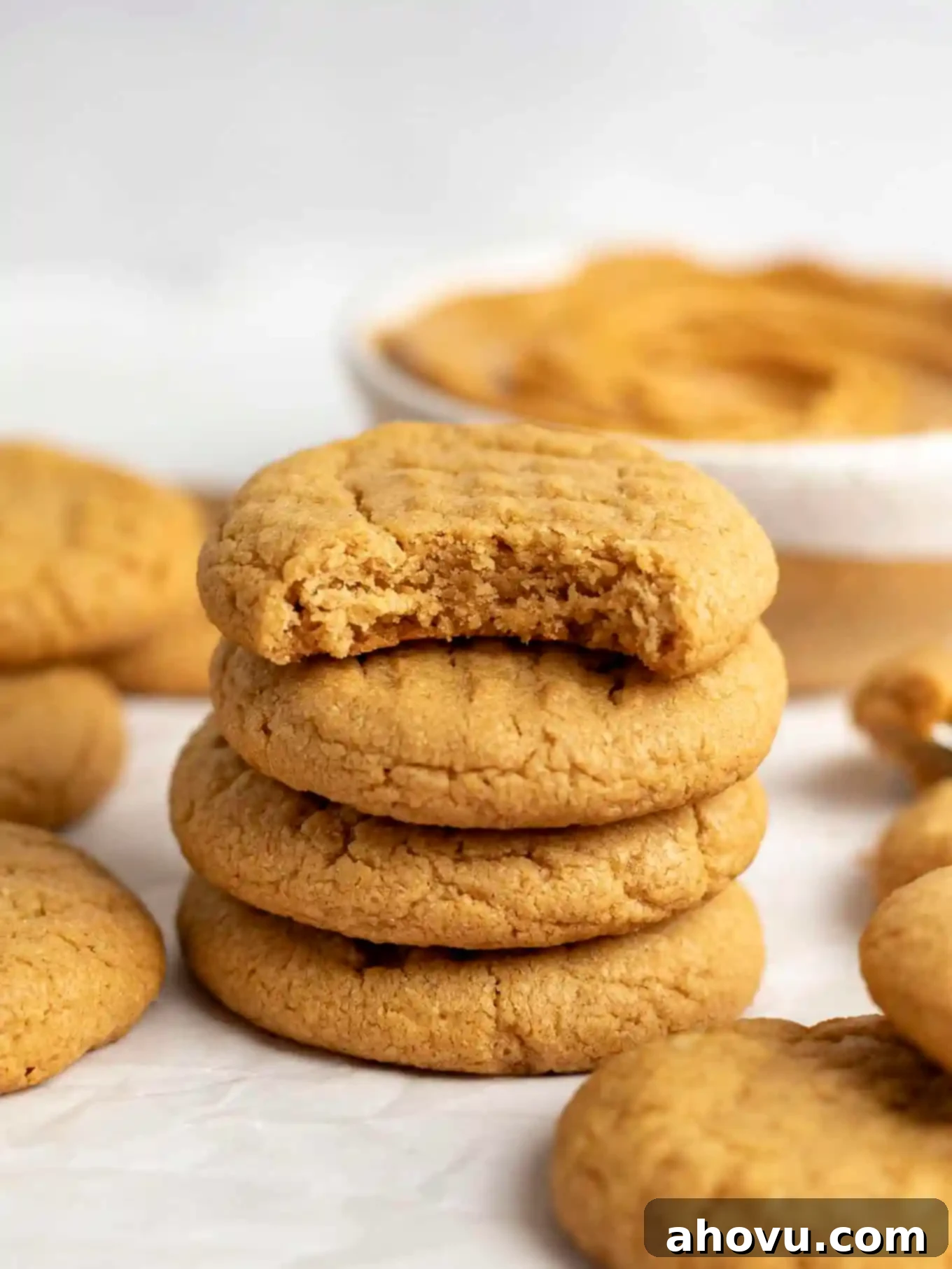A stack of four peanut butter cookies, with the top cookie missing a bite. 