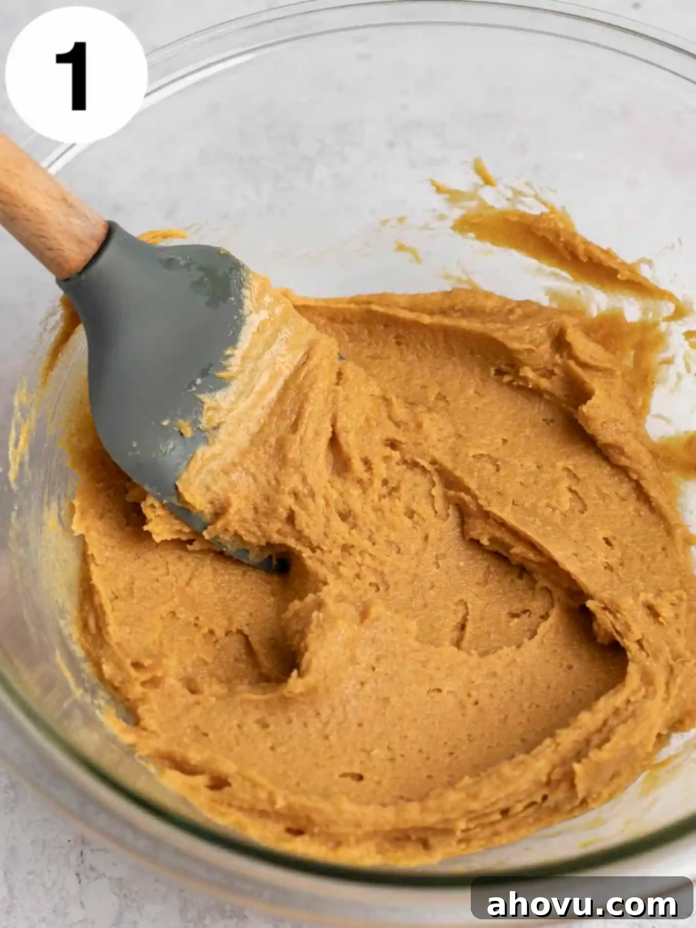 Peanut butter cookie dough in a glass mixing bowl, with a rubber spatula. 